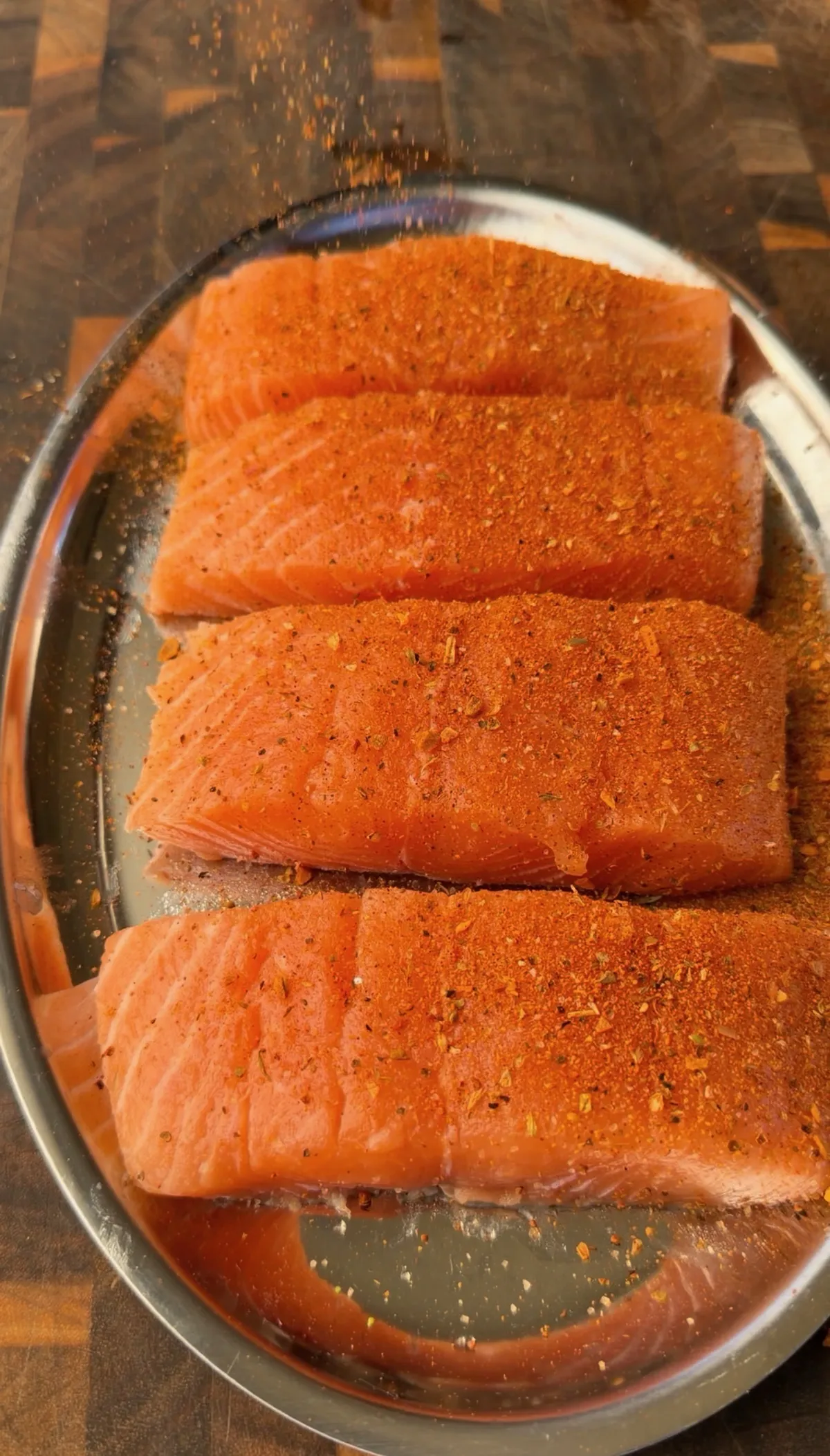 Three raw salmon portions generously coated with Cajun seasoning on a silver tray, ready to pan sear