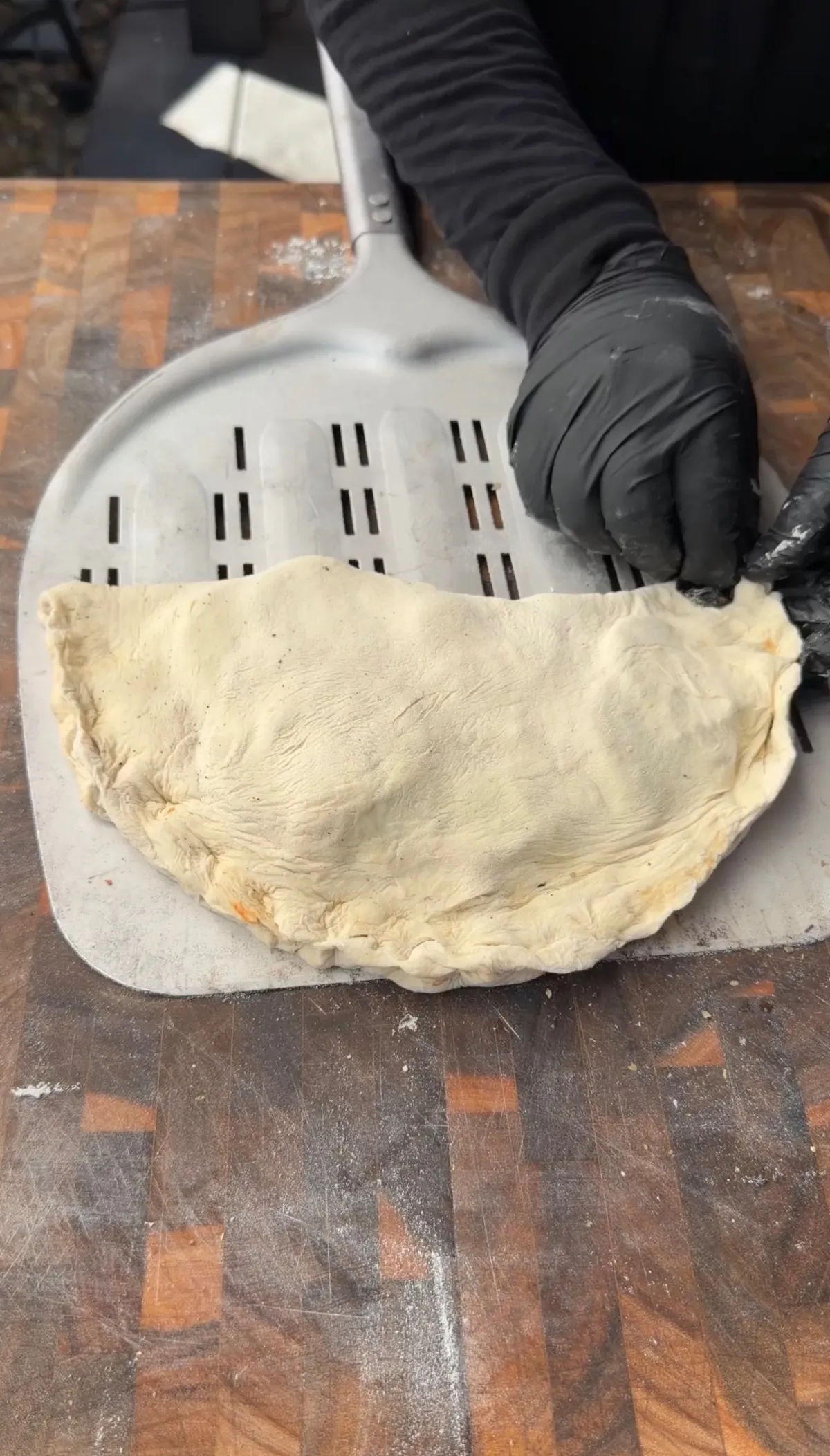 Folded and crimped pepperoni calzone on a perforated pizza peel, ready to bake