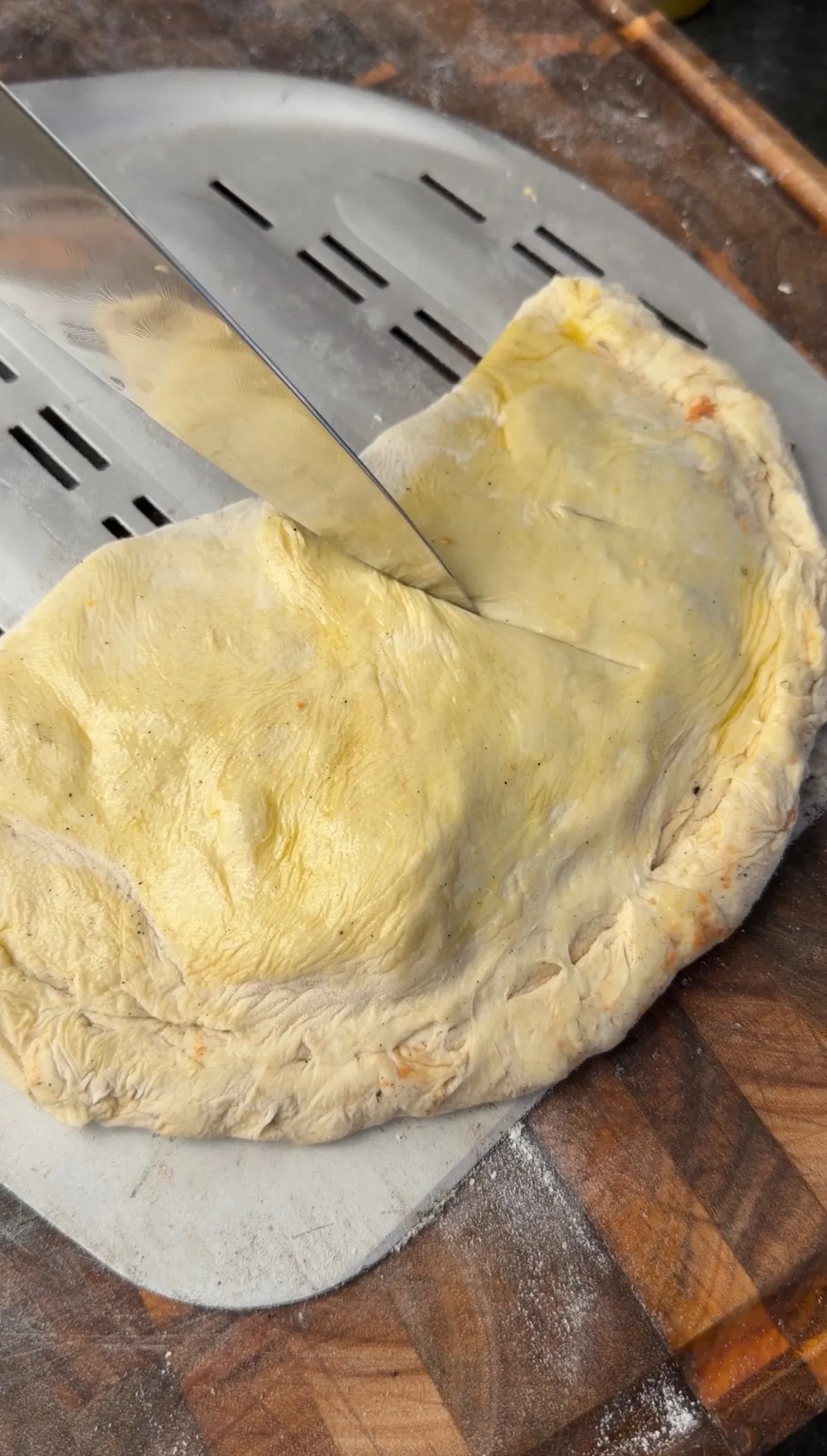 Folded and sealed pepperoni calzone with 3 venting slits cut on top, resting on a metal pizza pan