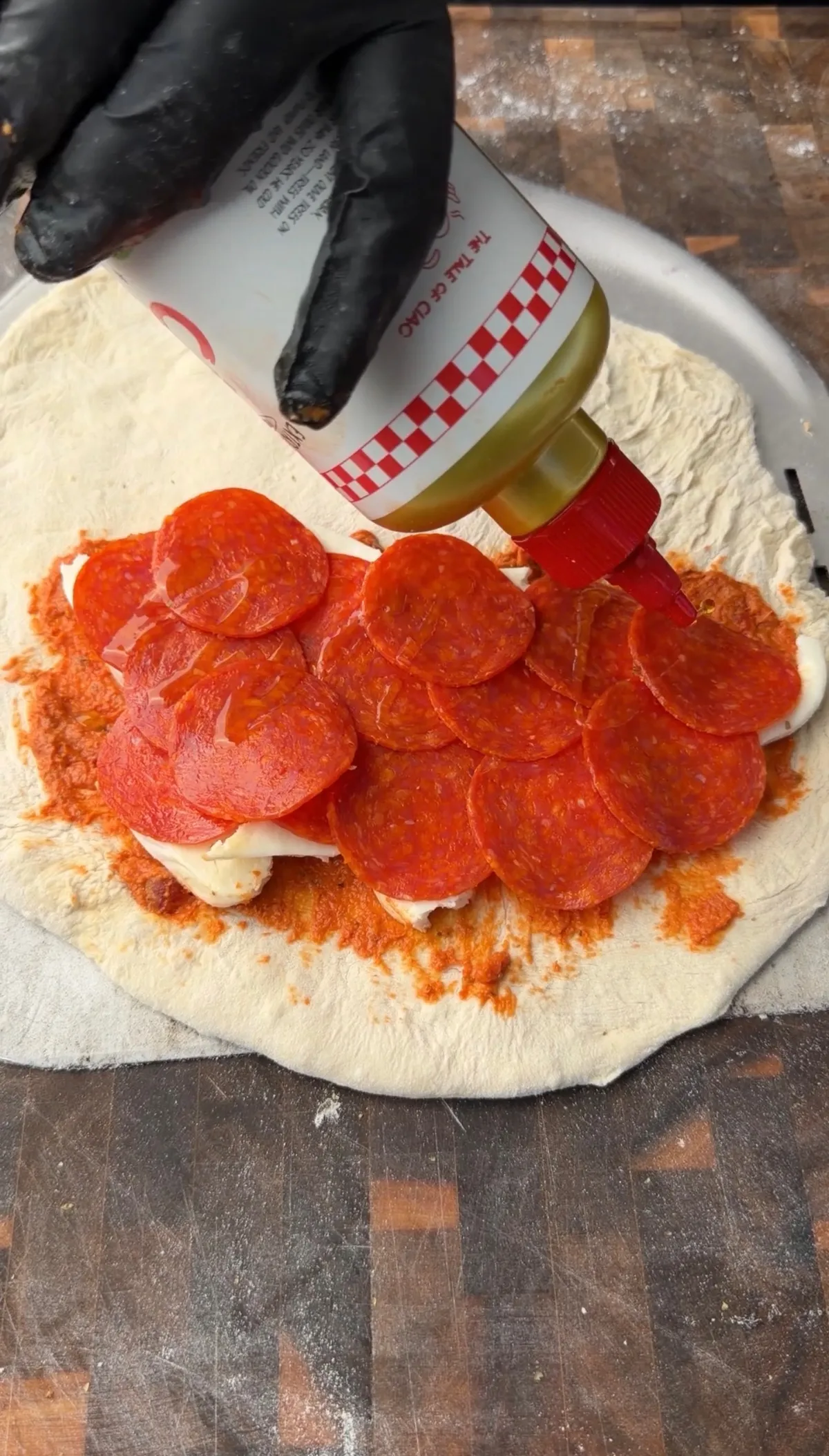 Drizzling olive oil over pepperoni and fresh mozzarella calzone filling on stretched pizza dough