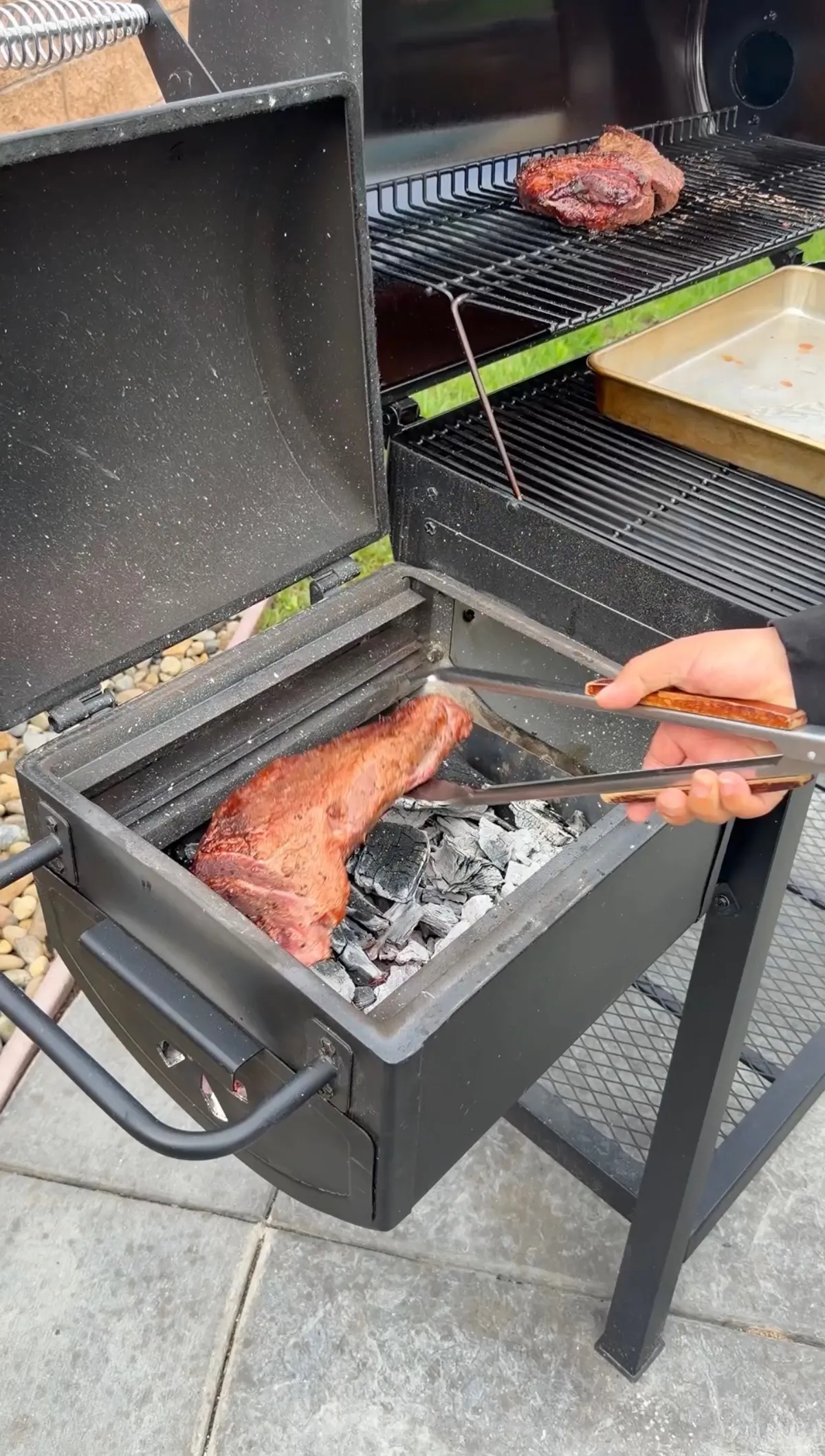 Tri-tip being seared directly over hot lump charcoal with tongs in Caveman-style reverse-sear technique