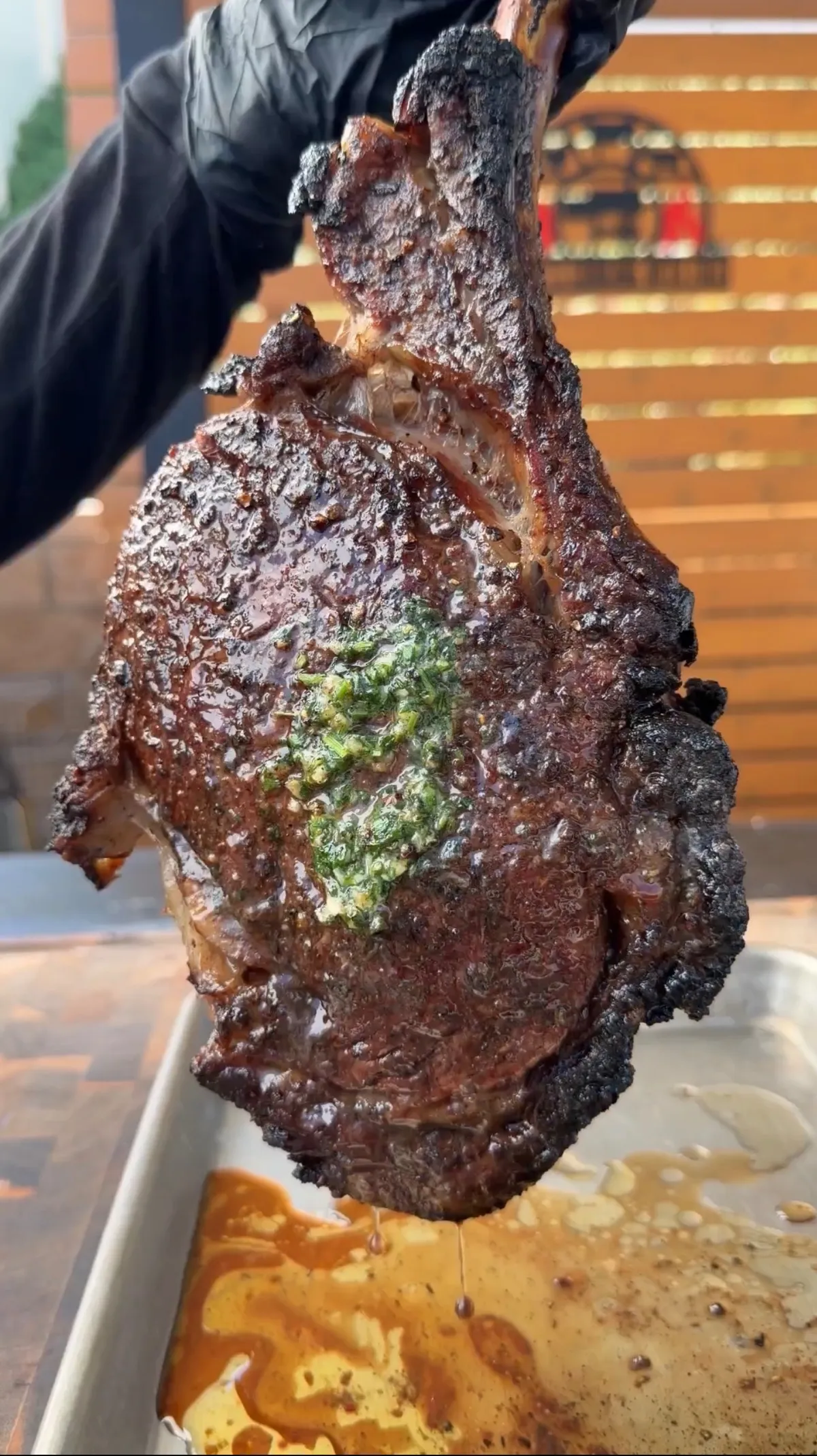 Smoked tomahawk steak held upright after caveman sear, with compound butter melting over charred crust, juices dripping