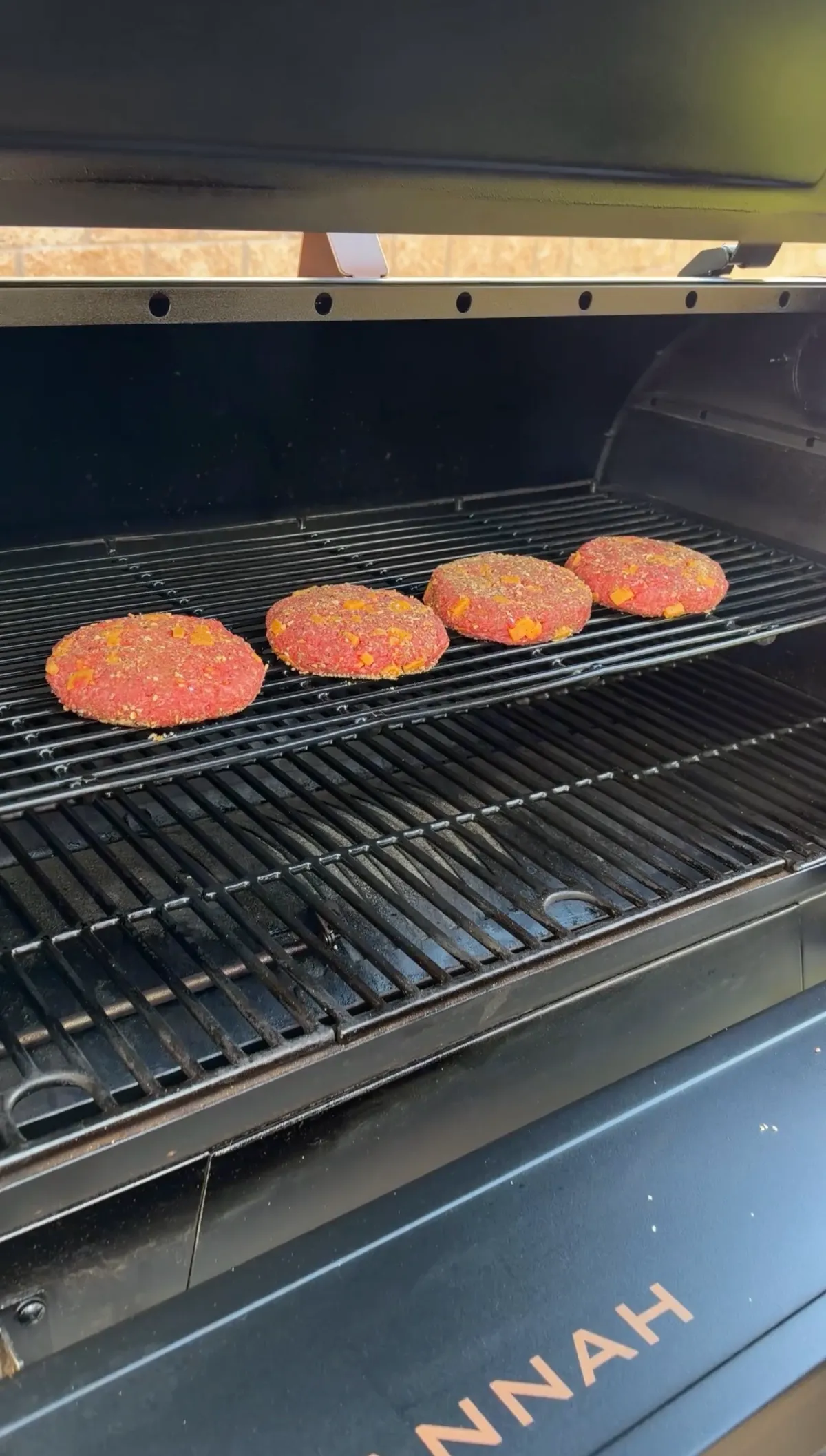 Four raw 85/15 ground beef and cubed cheddar stuffed burger patties on a smoker grill rack at 250°F