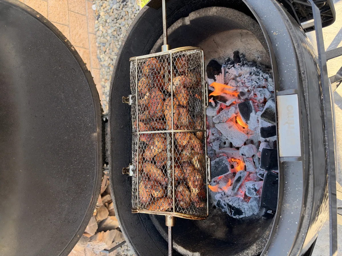Chicken wings loaded in a rotisserie basket spinning over hot charcoal at 300–350°F until golden and crispy