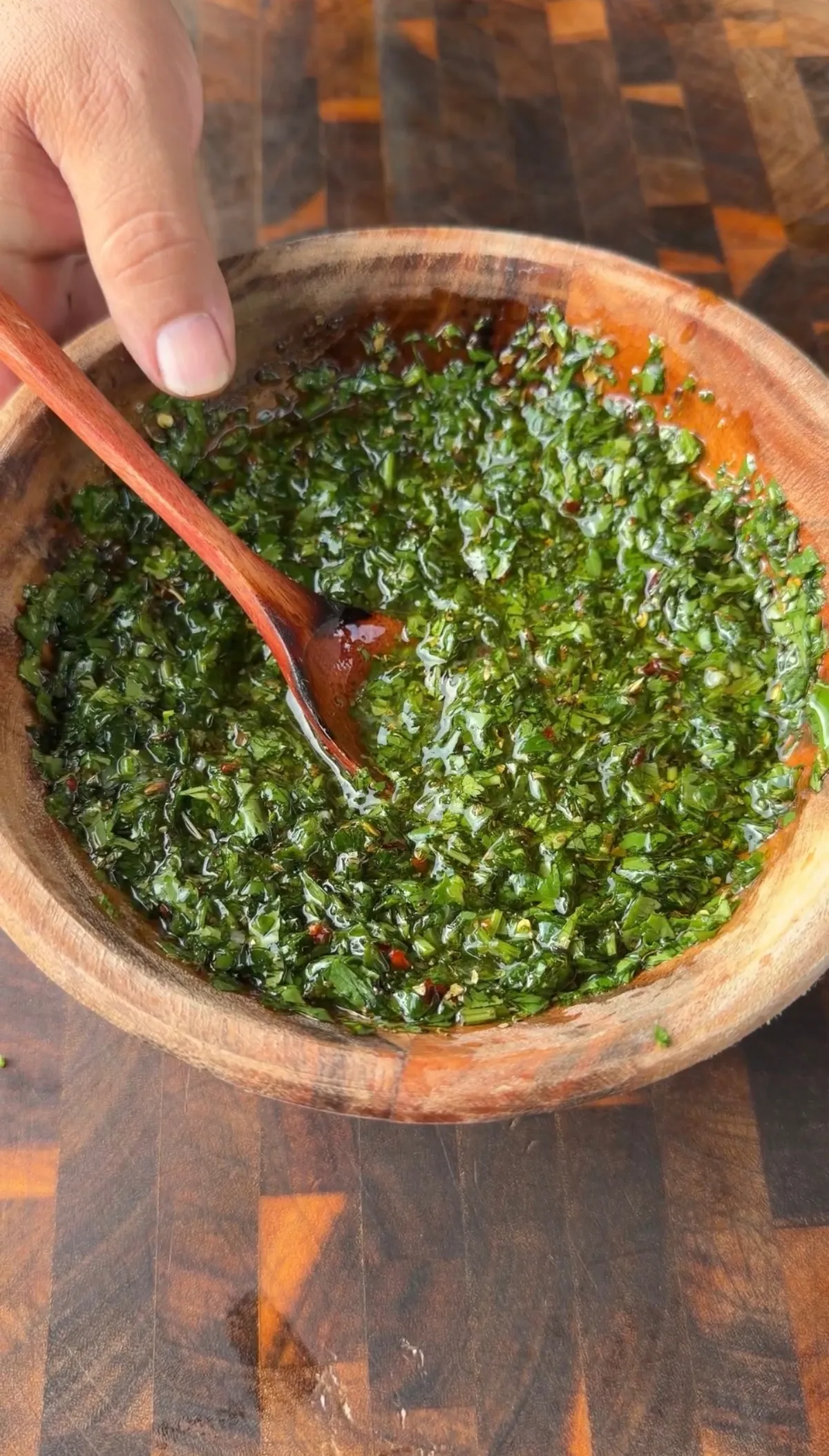 Fresh chimichurri with parsley, cilantro, garlic, olive oil, and red pepper flakes being stirred in a wooden bowl