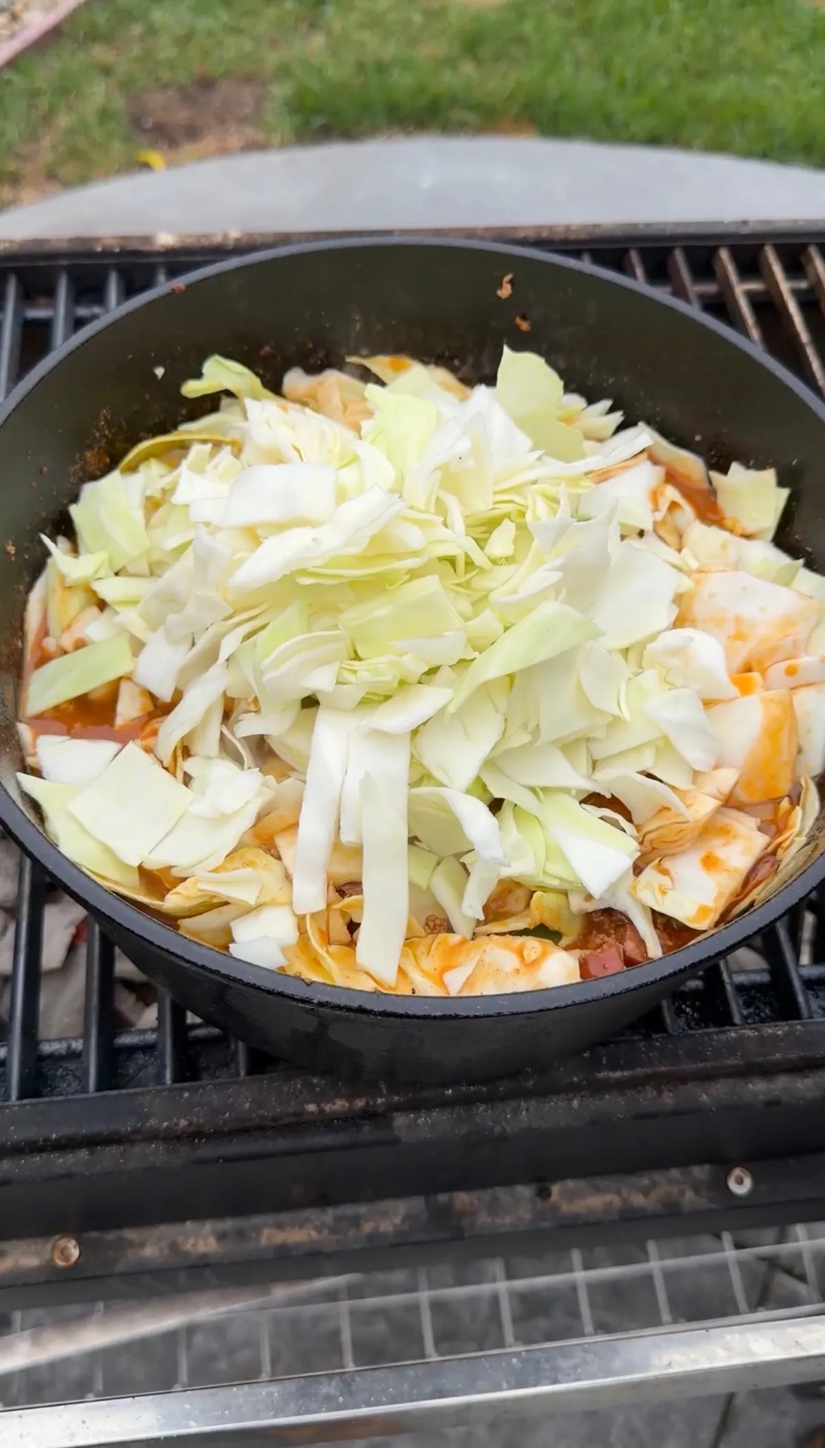 Roughly chopped green cabbage piled into a Dutch oven over a grill grate on top of Creole-seasoned meat and sauce
