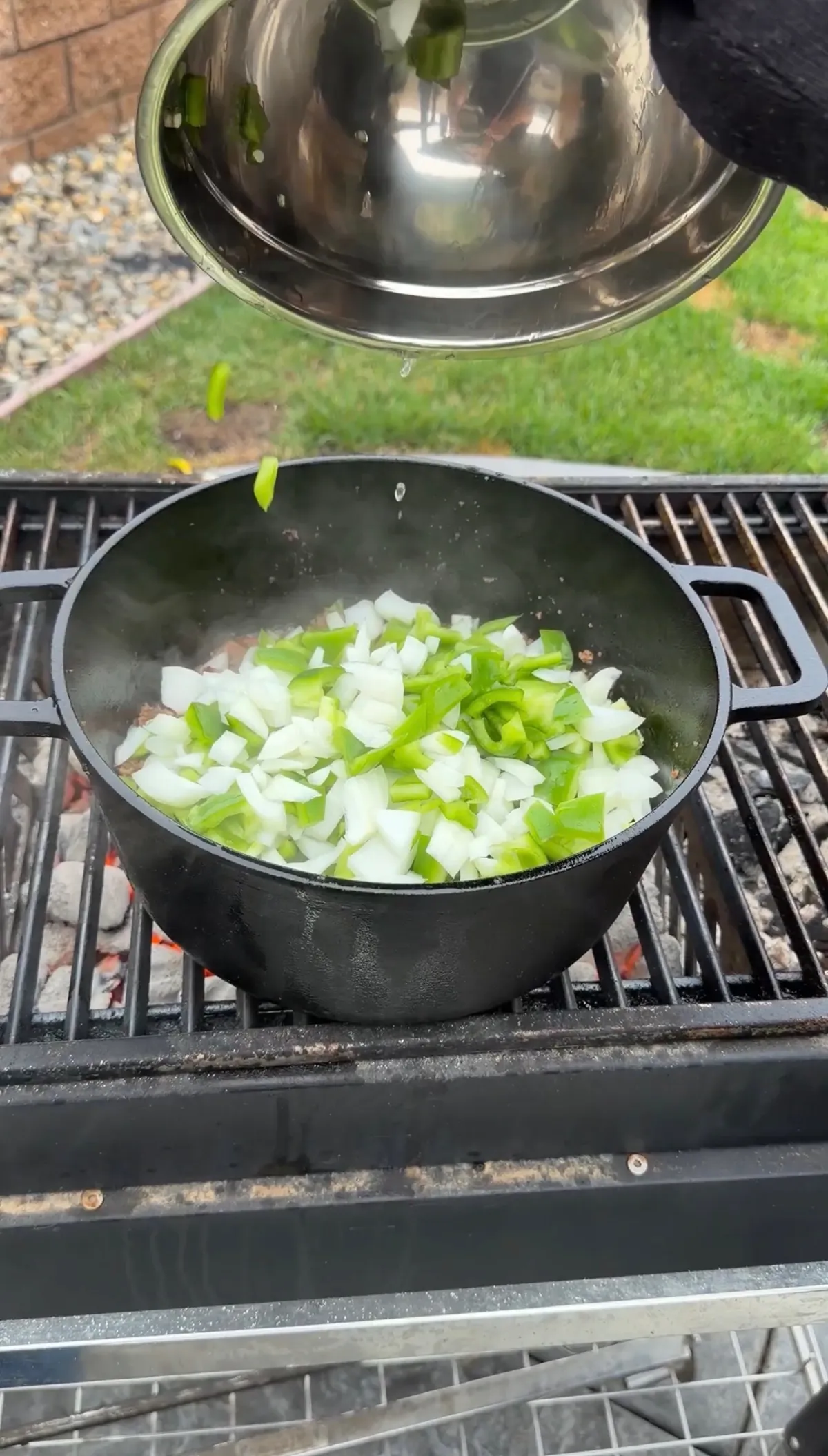 Roughly chopped white onion and green bell pepper added to a cast iron Dutch oven on a charcoal grill