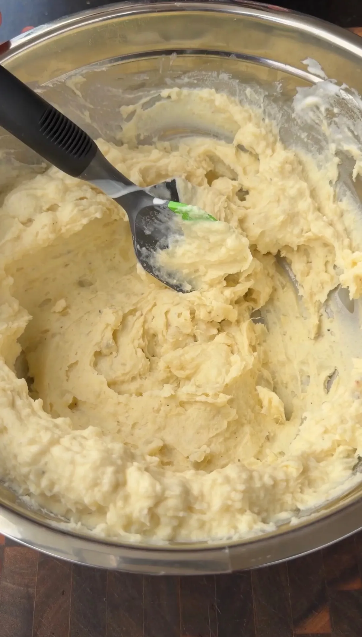 Creamy mashed russet potatoes with butter and heavy cream being mixed in a stainless steel bowl