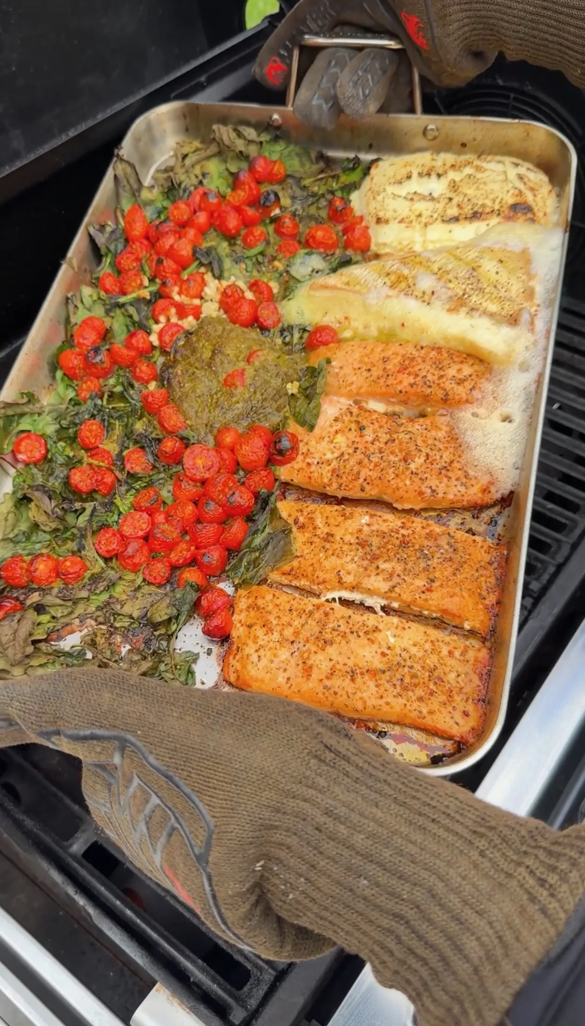 Salmon portions with roasted cherry tomatoes, wilted spinach, pesto, Brie, and cream cheese bubbling in a grill-safe pan