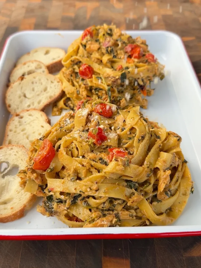 Creamy pesto salmon fettuccine with wilted spinach, cherry tomatoes, and Brie sauce, served with toasted bread slices