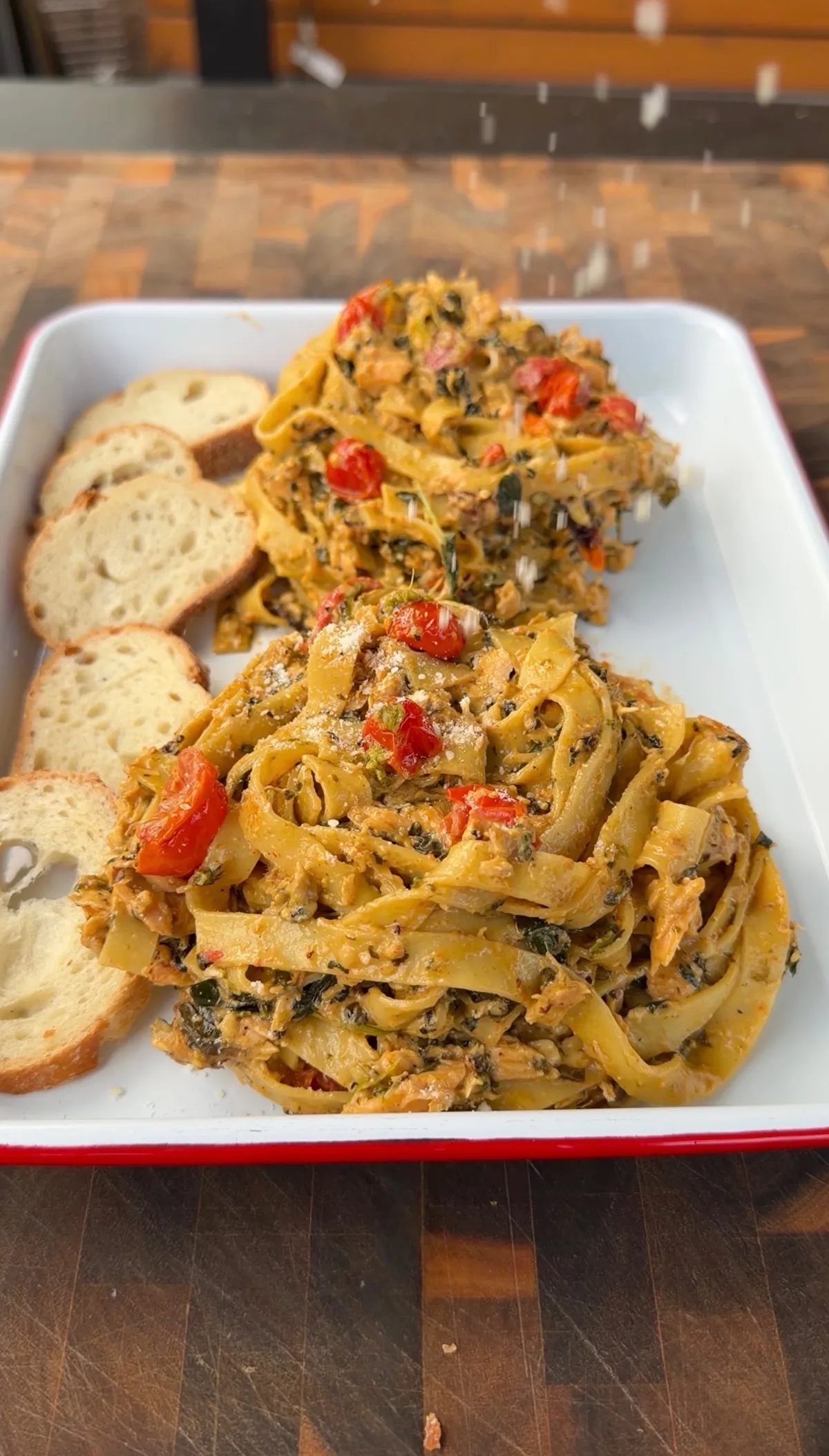 Creamy pesto salmon fettuccine with wilted spinach, cherry tomatoes, and Brie sauce, served with toasted bread slices