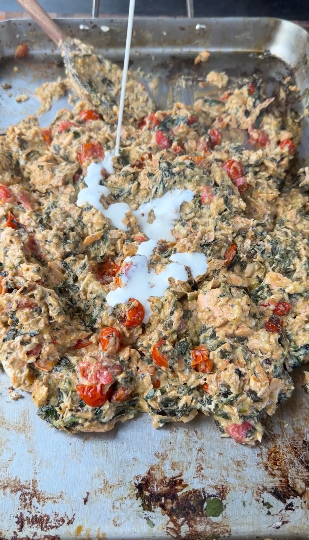 Heavy cream being poured over baked salmon, Brie, cream cheese, pesto, spinach, and cherry tomatoes in a roasting pan