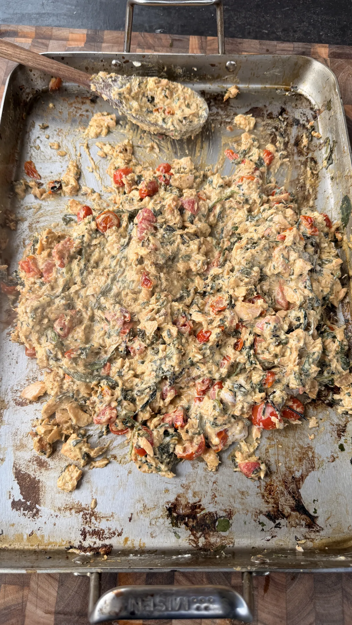 Creamy pesto salmon sauce with cherry tomatoes and spinach mixed together in a stainless steel baking pan