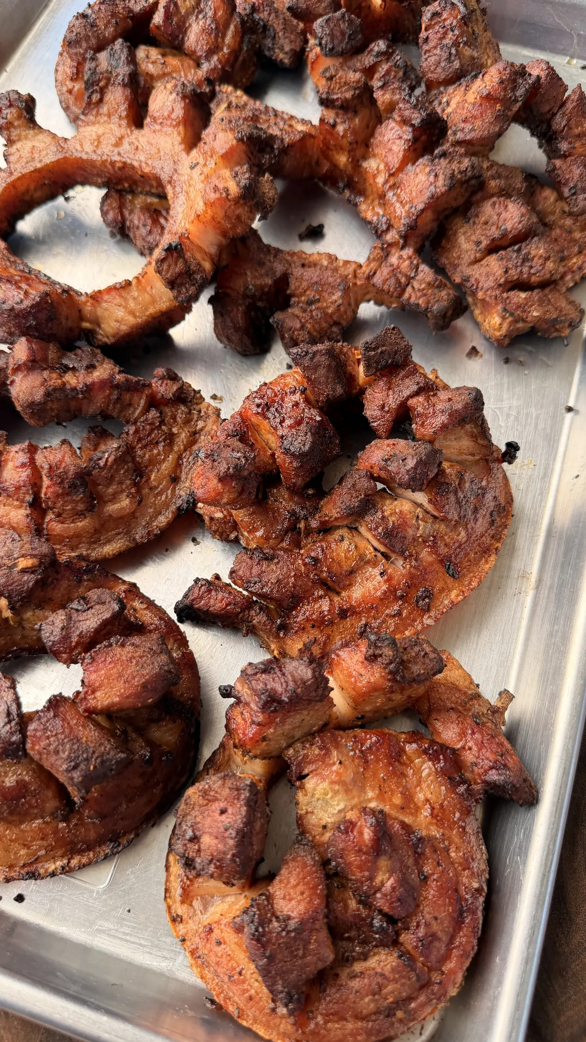 Crispy chicharrón pinwheels with golden rendered pork belly skin on a metal tray after grilling over charcoal