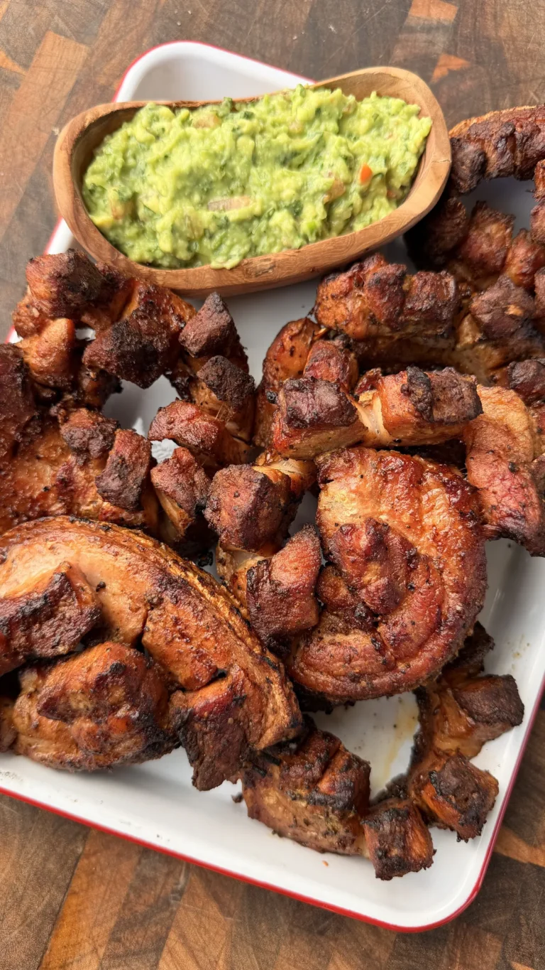 Grilled chicharrón pinwheels with crispy skin on a white platter served with fresh guacamole in a wooden bowl
