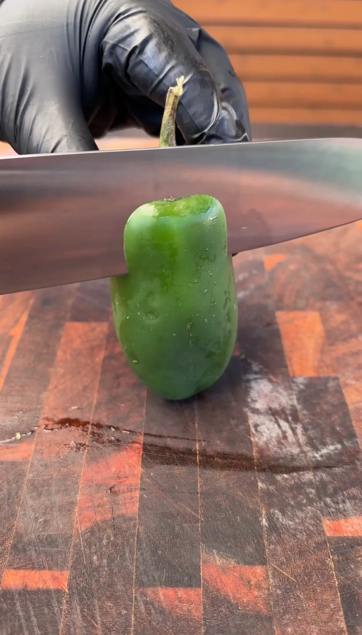 A large jalapeño being cut into a boat shape from the stem end on a wood cutting board with a chef's knife