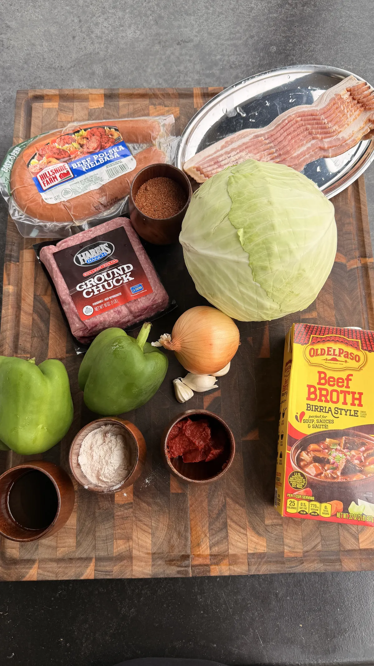 Dirty cabbage recipe ingredients: ground chuck, bacon, kielbasa, cabbage, bell pepper, onion, garlic, tomato paste, flour, Creole seasoning, and beef broth
