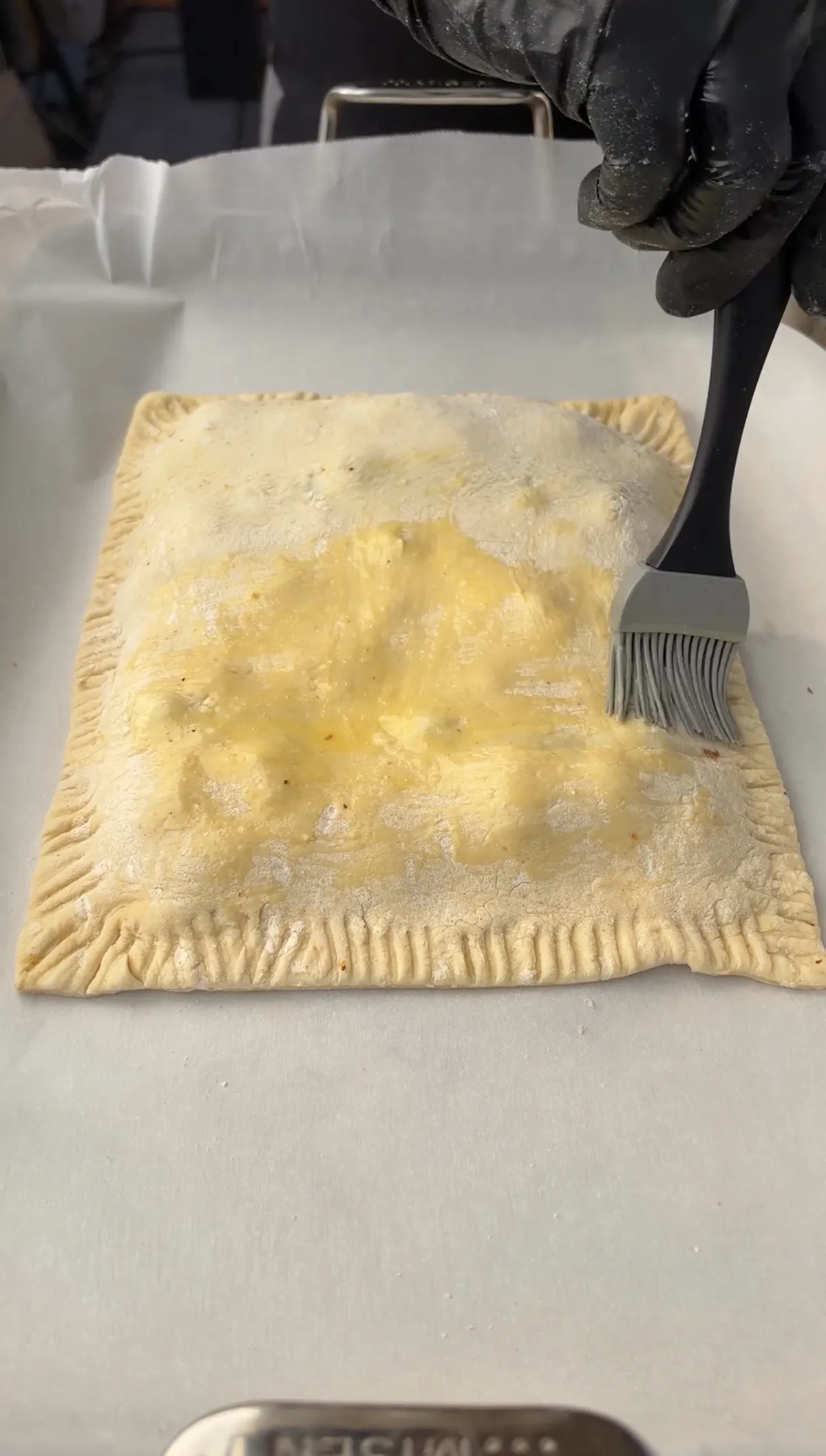 Egg wash being brushed over crimped puff pastry smoked brisket hot pocket before baking