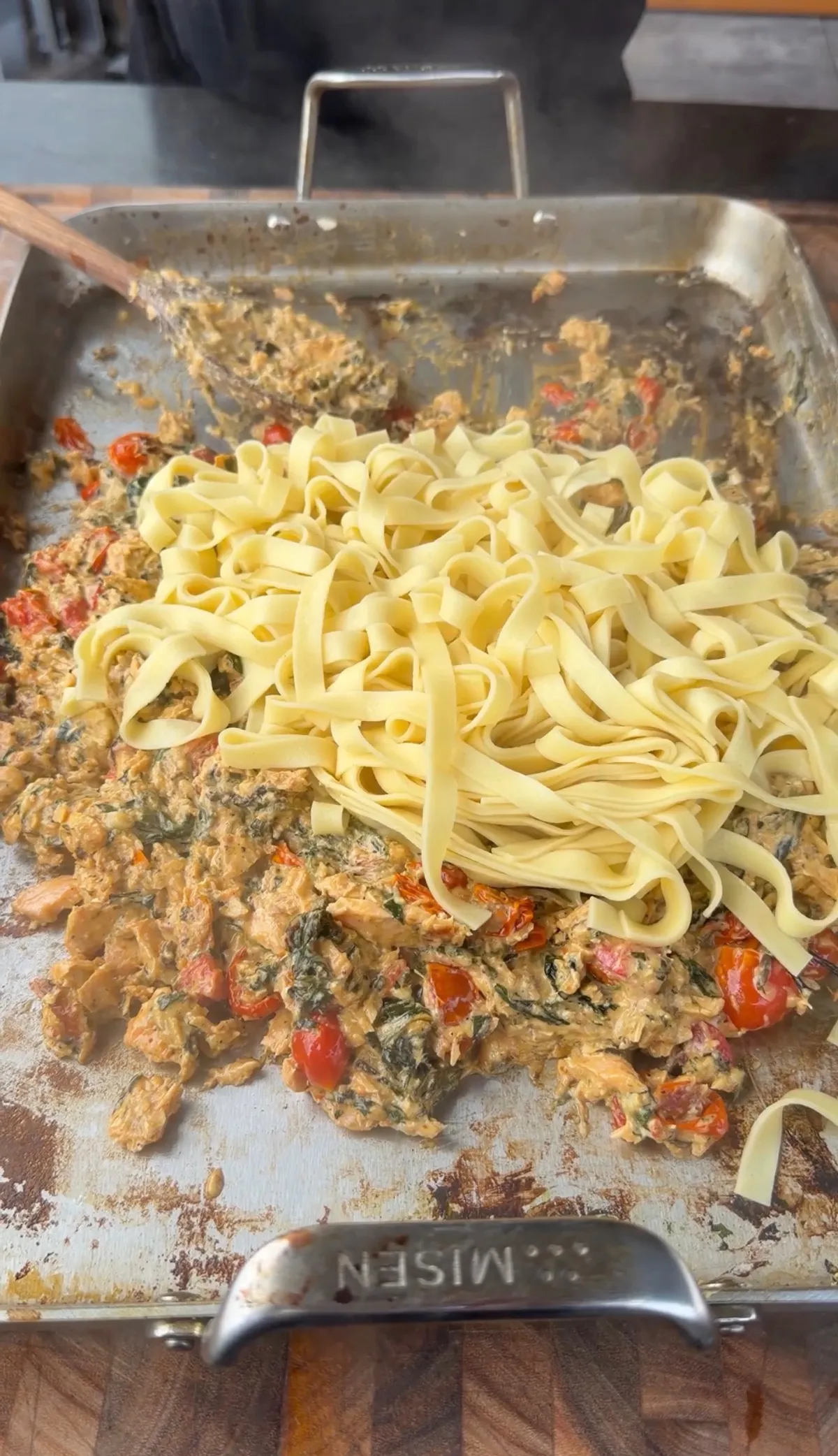 Cooked fettuccine added to creamy pesto salmon sauce with cherry tomatoes and spinach in a Misen baking pan