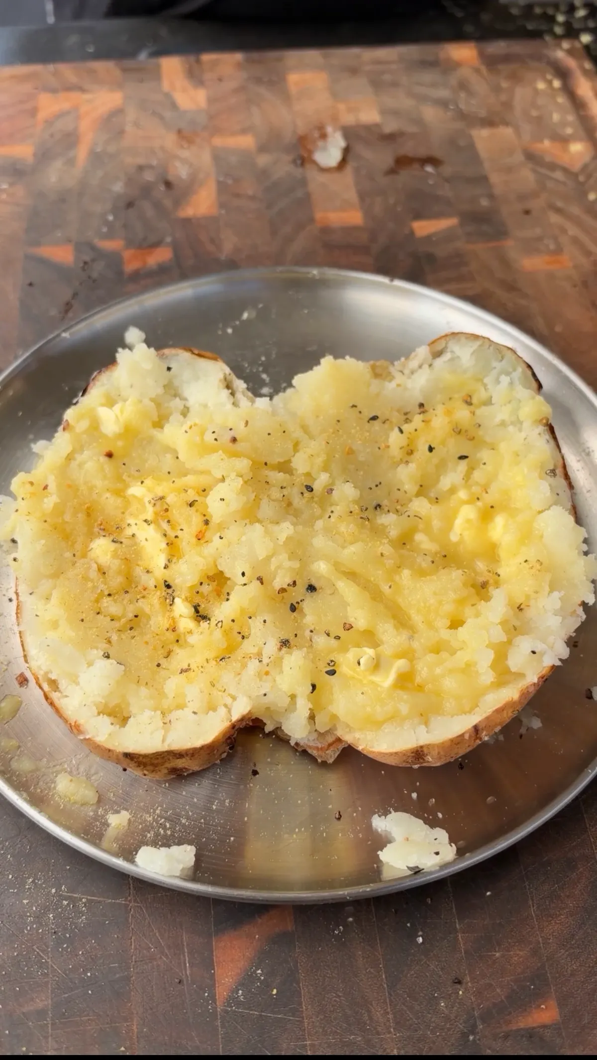 Russet potato halves fluffed with fork, melted butter, and garlic pepper seasoning on a silver plate