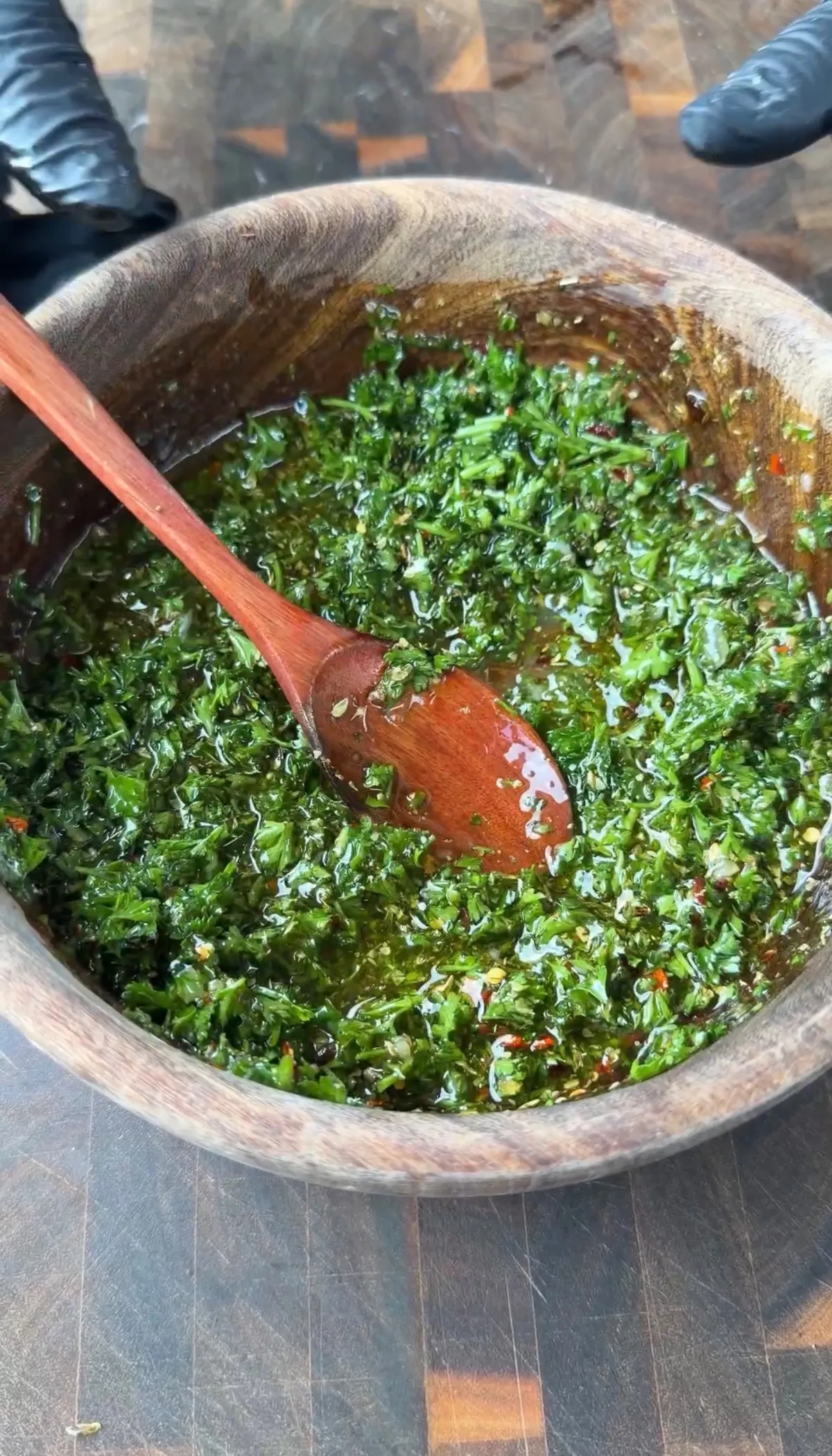 Fresh chimichurri with parsley, oregano, red pepper flakes, and olive oil mixed in a wooden bowl with a wooden spoon