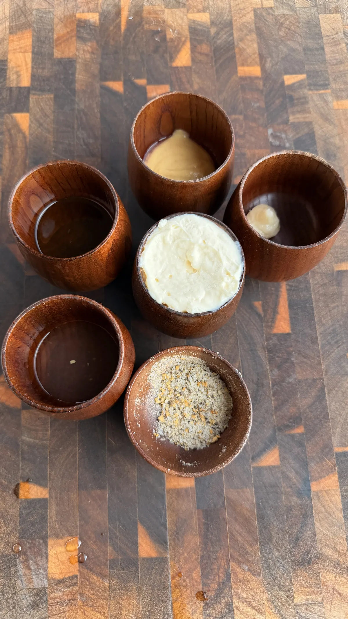 Wooden bowls with garlic aioli, Dijon mustard, chimichurri, and seasoning blend for tri-tip sandwich on cutting board