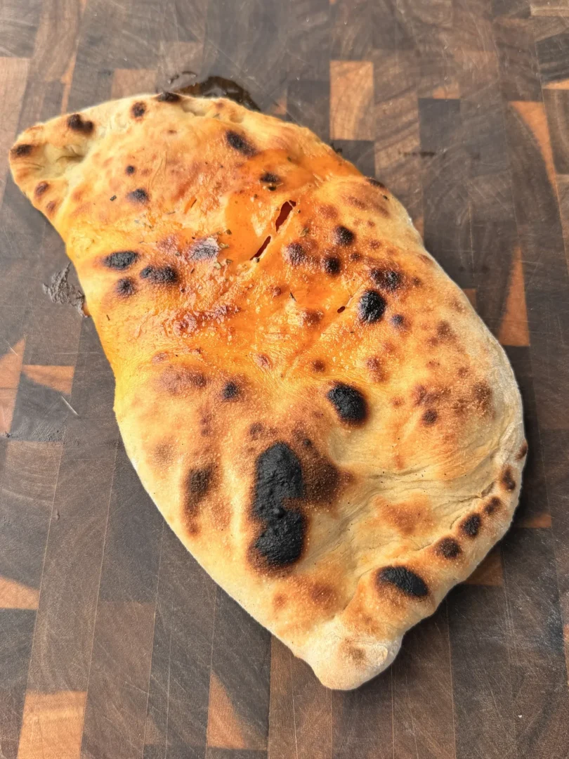 Baked pepperoni calzone with golden-brown crispy crust and char marks on a wooden cutting board