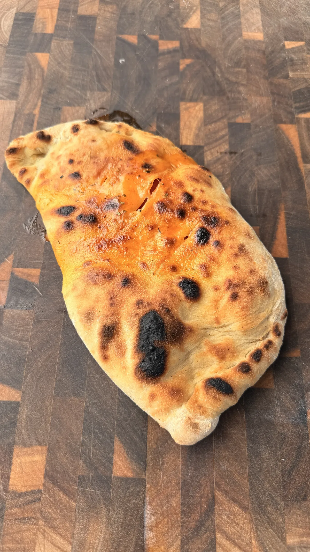 Baked pepperoni calzone with golden-brown crispy crust and char marks on a wooden cutting board