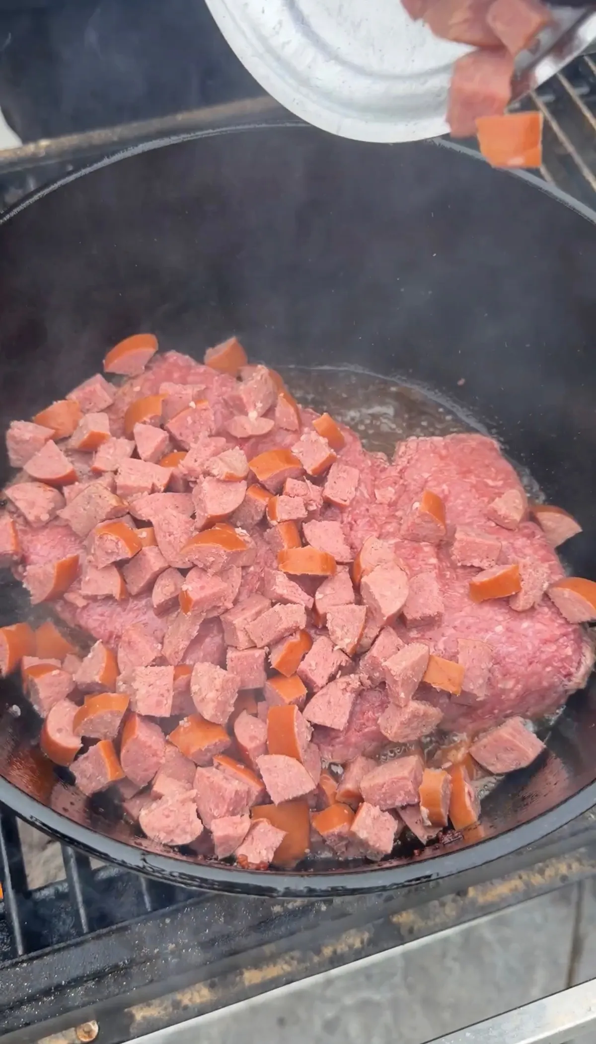 Ground chuck and quartered kielbasa rounds browning together in bacon fat in a large black Dutch oven