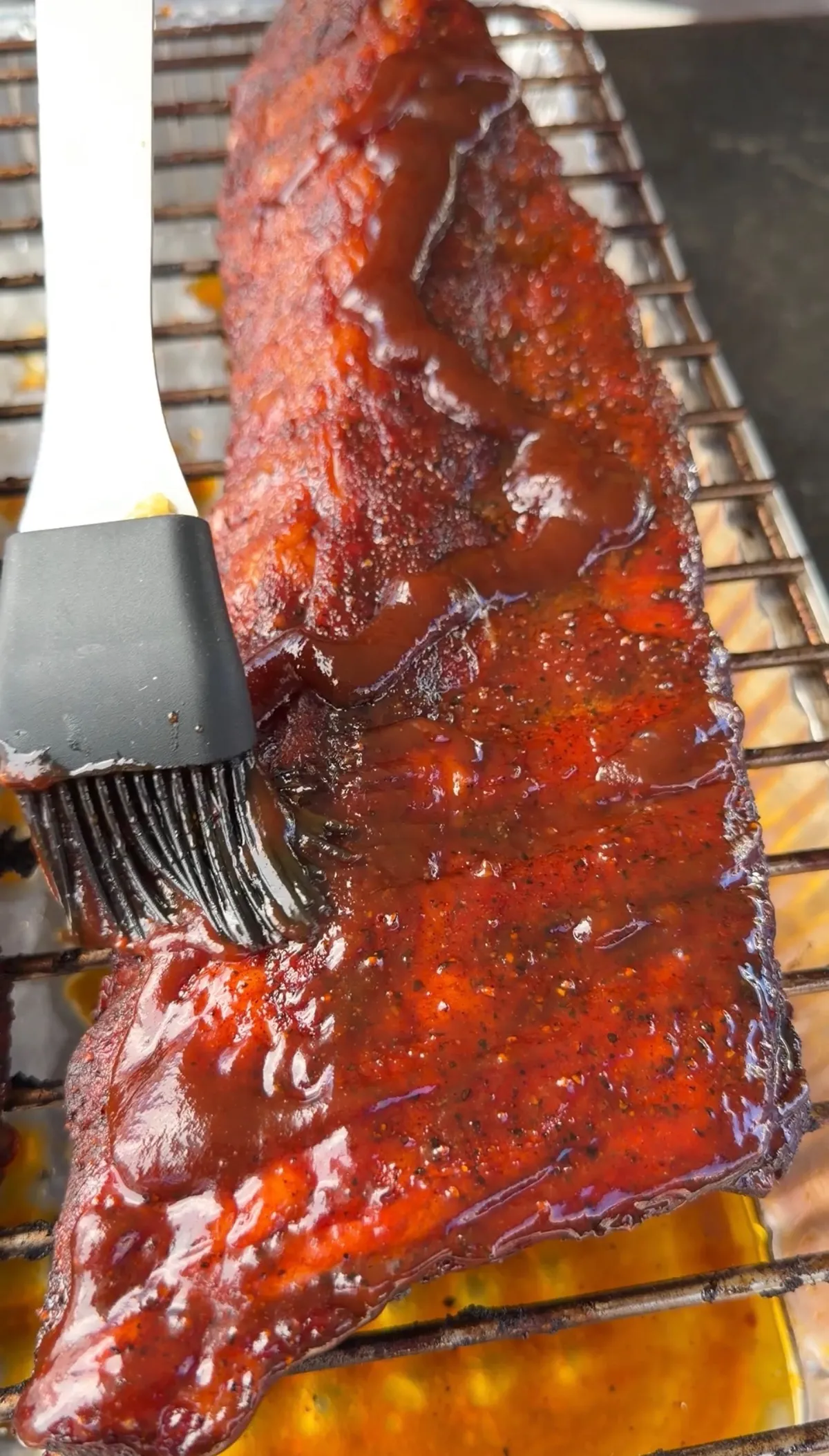 Brushing honey BBQ sauce glaze onto applewood-smoked chipotle baby back ribs on smoker grate