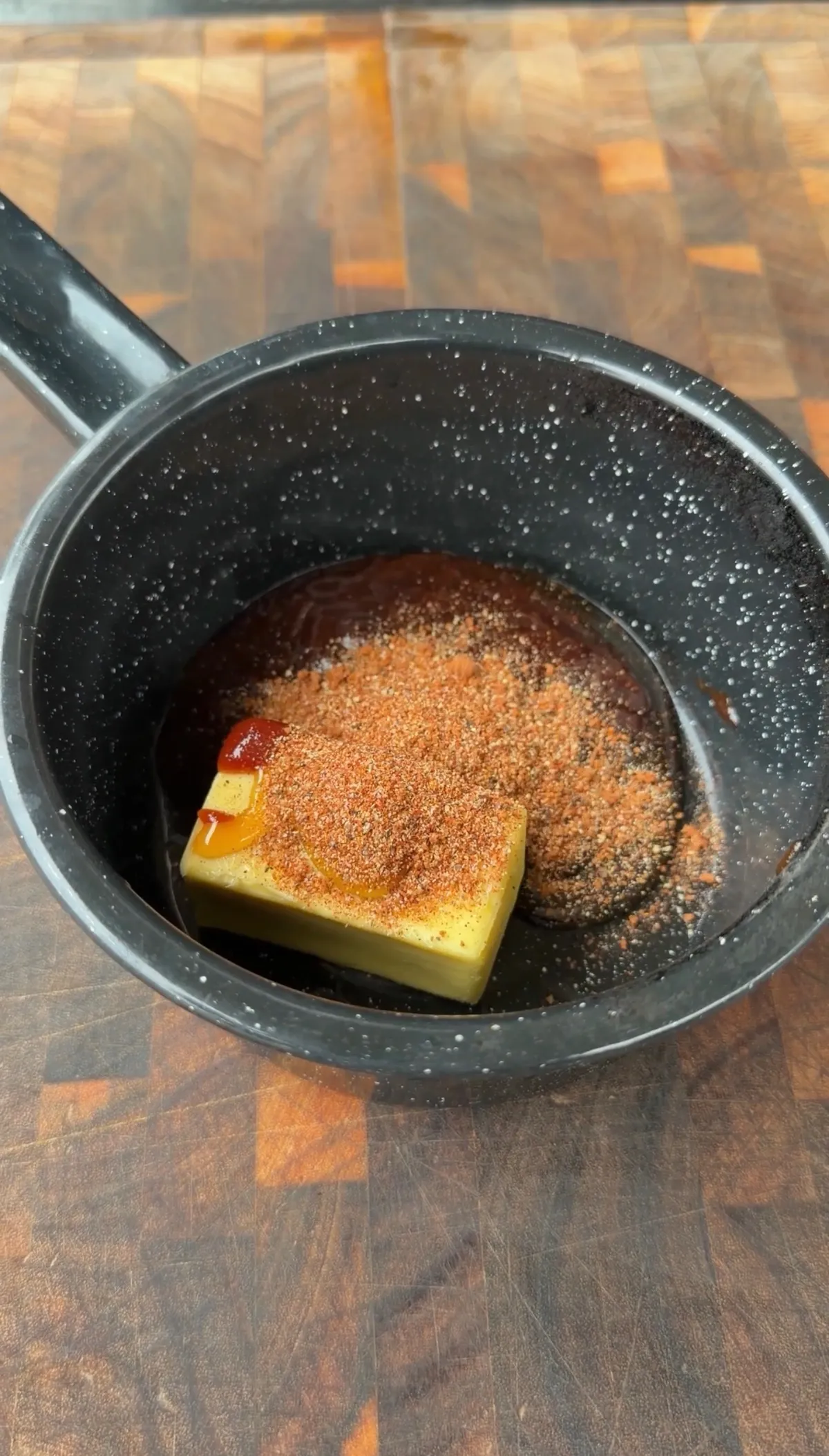 Butter, honey BBQ sauce, and chipotle seasoning in a small black saucepan for honey chipotle glaze