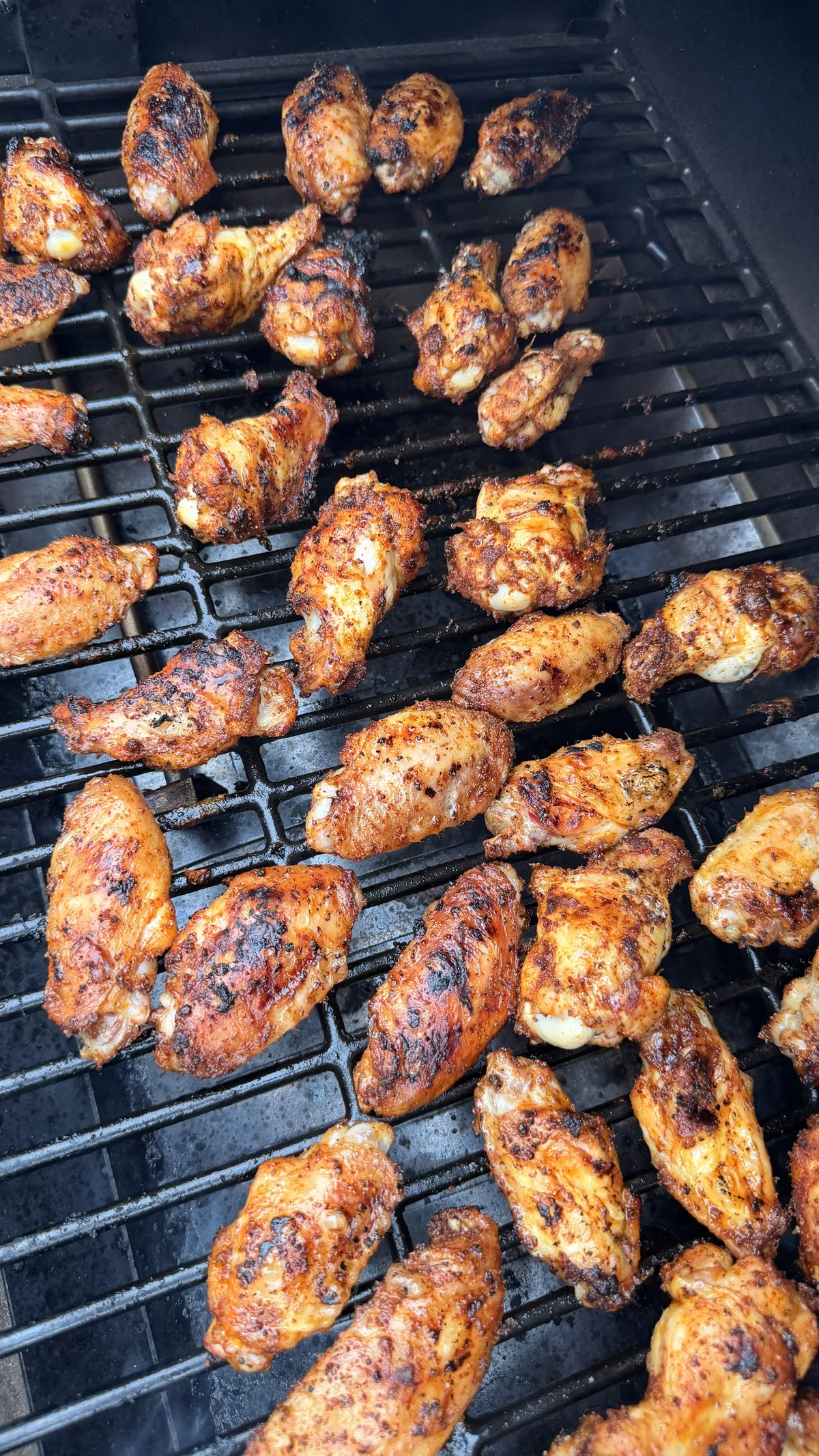 Chipotle-seasoned chicken wings cooking on a smoker grill at 350°F, golden-brown with crispy charred skin