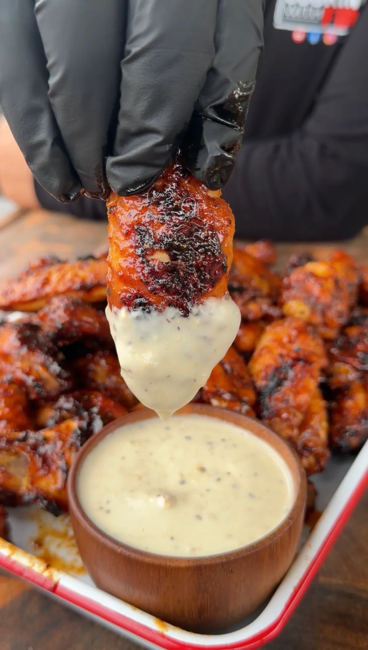 Glazed honey chipotle smoked chicken wing being dipped in ranch dressing over a tray of wings