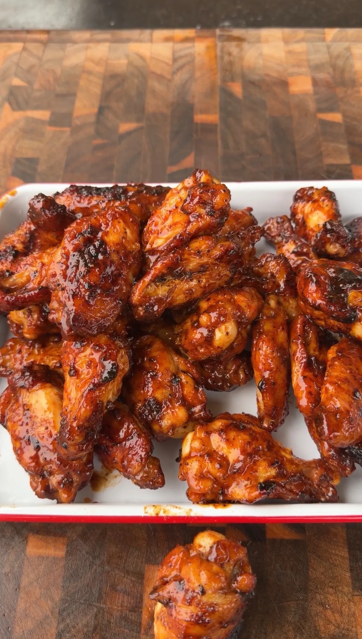 Honey chipotle glazed smoked chicken wings piled in a white dish on a wood cutting board