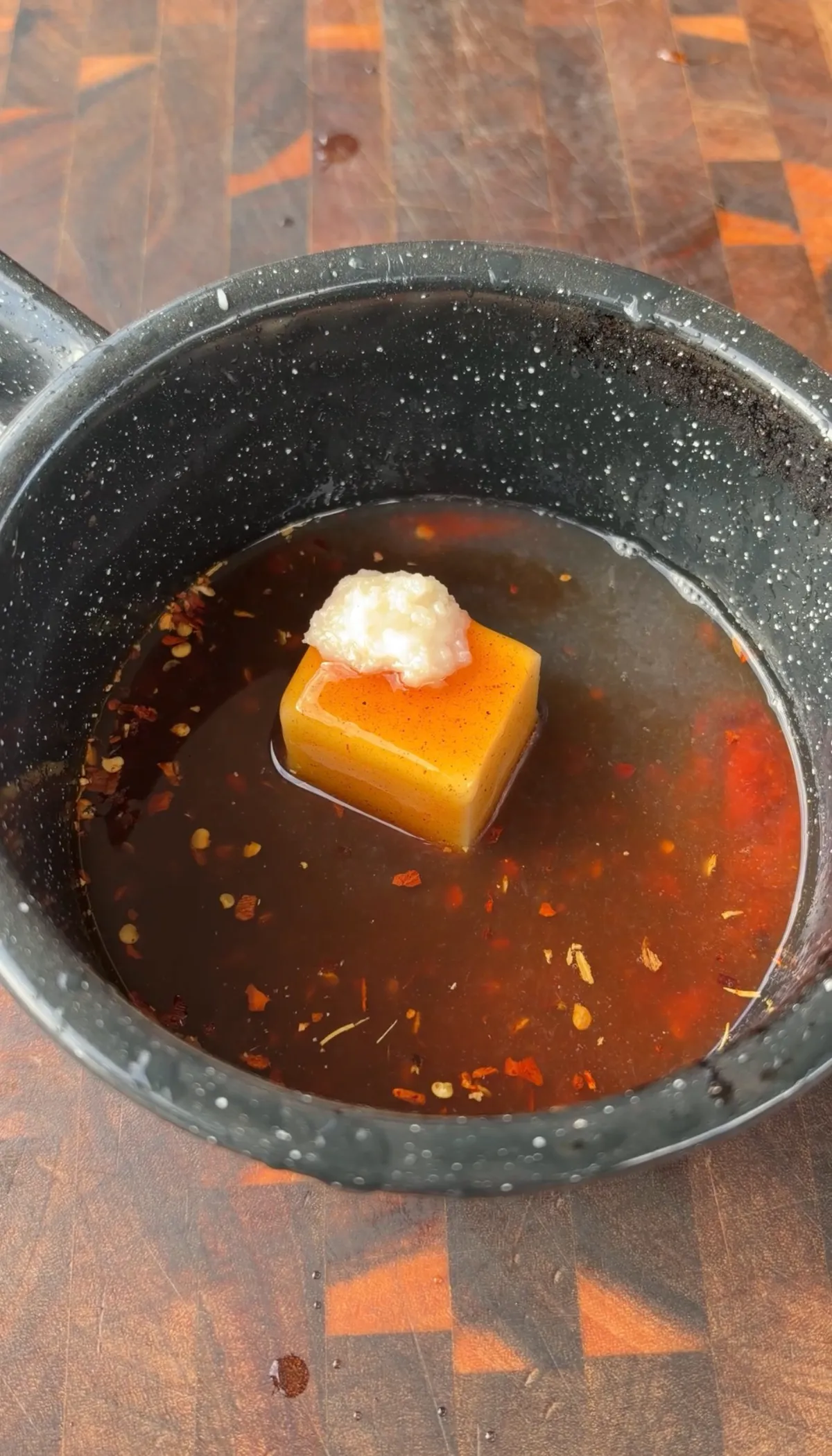 Hot honey lime sauce with red pepper flakes and minced garlic melting together in a dark saucepan