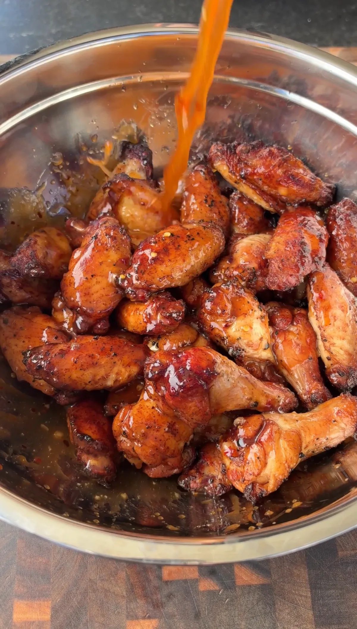 Crispy rotisserie chicken wings being tossed in hot honey lime sauce in a stainless steel bowl