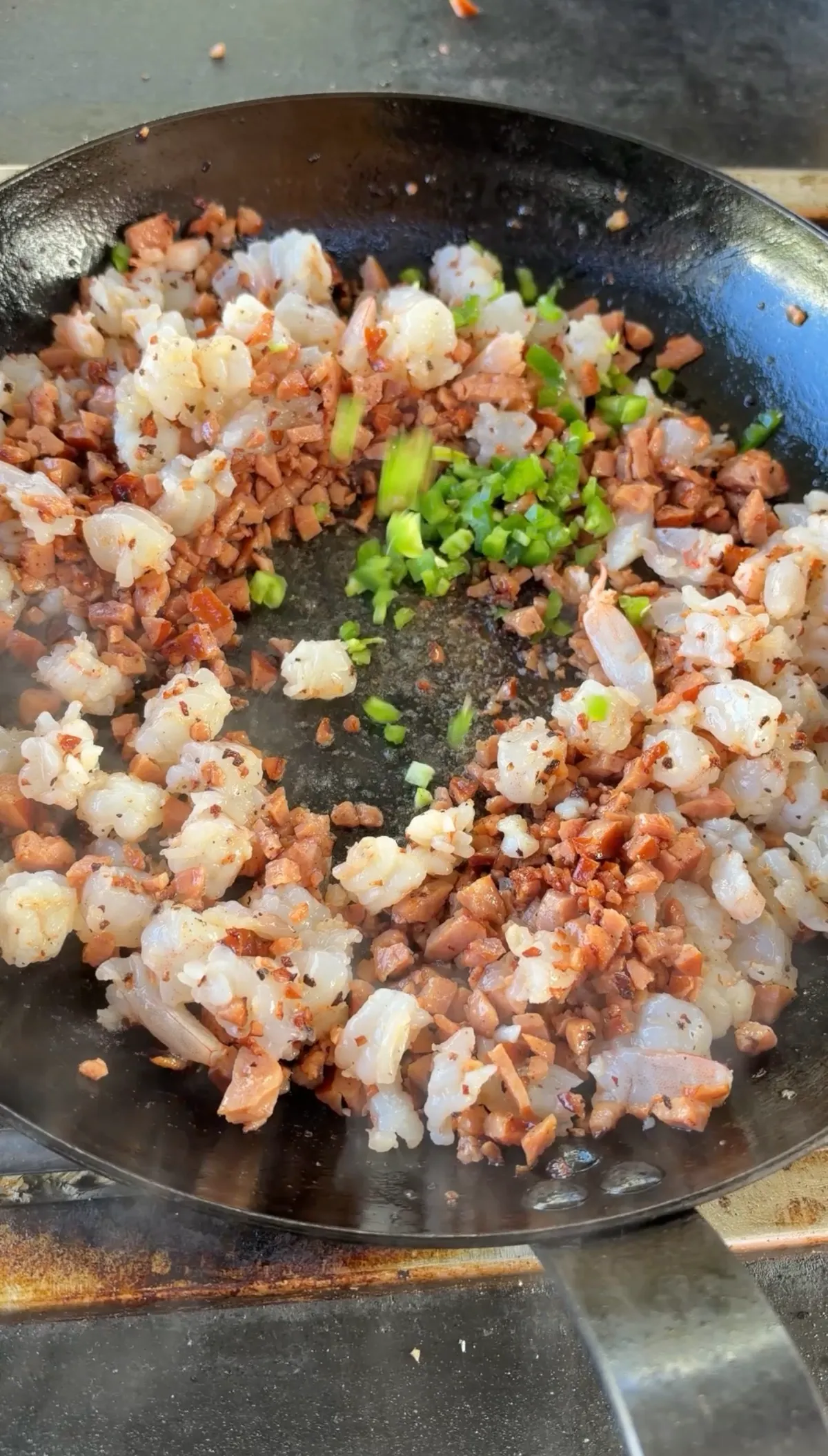 Diced kielbasa, shrimp pieces, and finely diced jalapeño cooking together in a black skillet