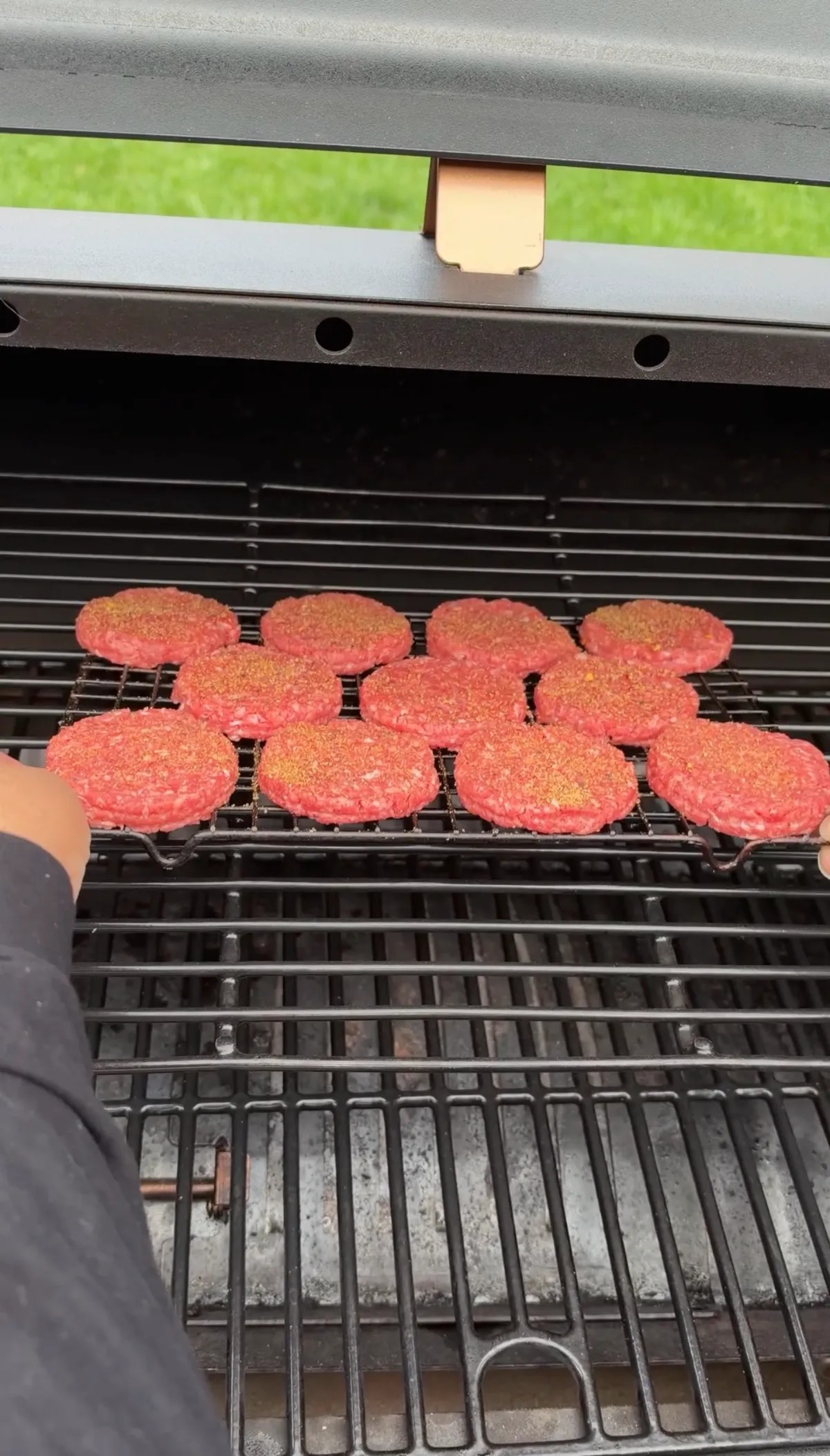 Eight mini 85/15 ground beef patties seasoned with Bear Mountain Barbecue Tailgating Blend on a wire rack inside a pellet smoker at 250°F