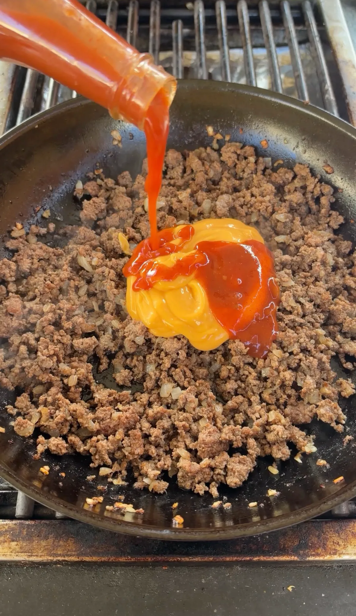 Taco Bell Mild Hot Sauce poured over nacho cheese and seasoned ground beef with onion in a skillet