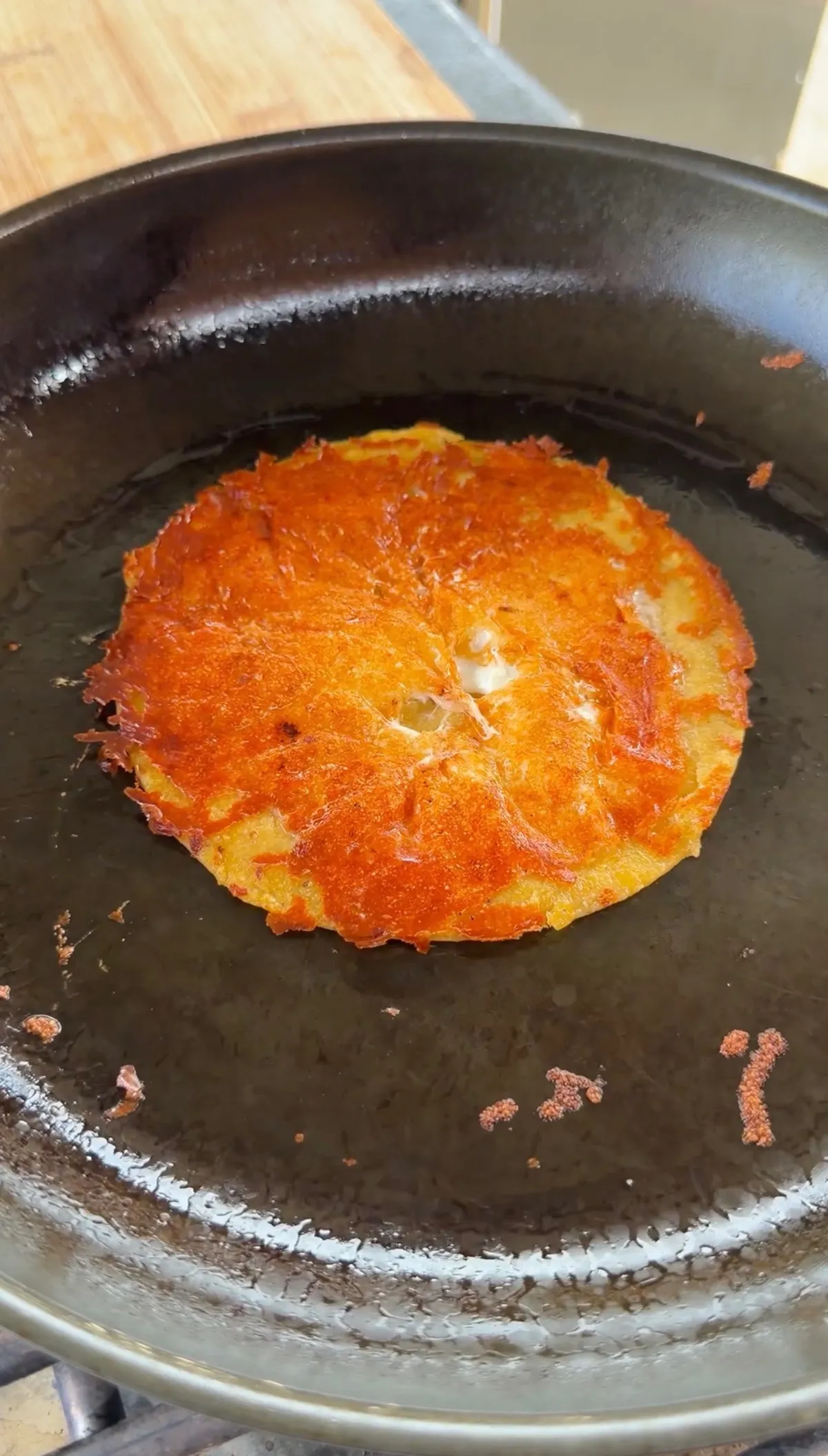 Shredded Oaxaca cheese crisping and browning around a corn tortilla in a nonstick pan