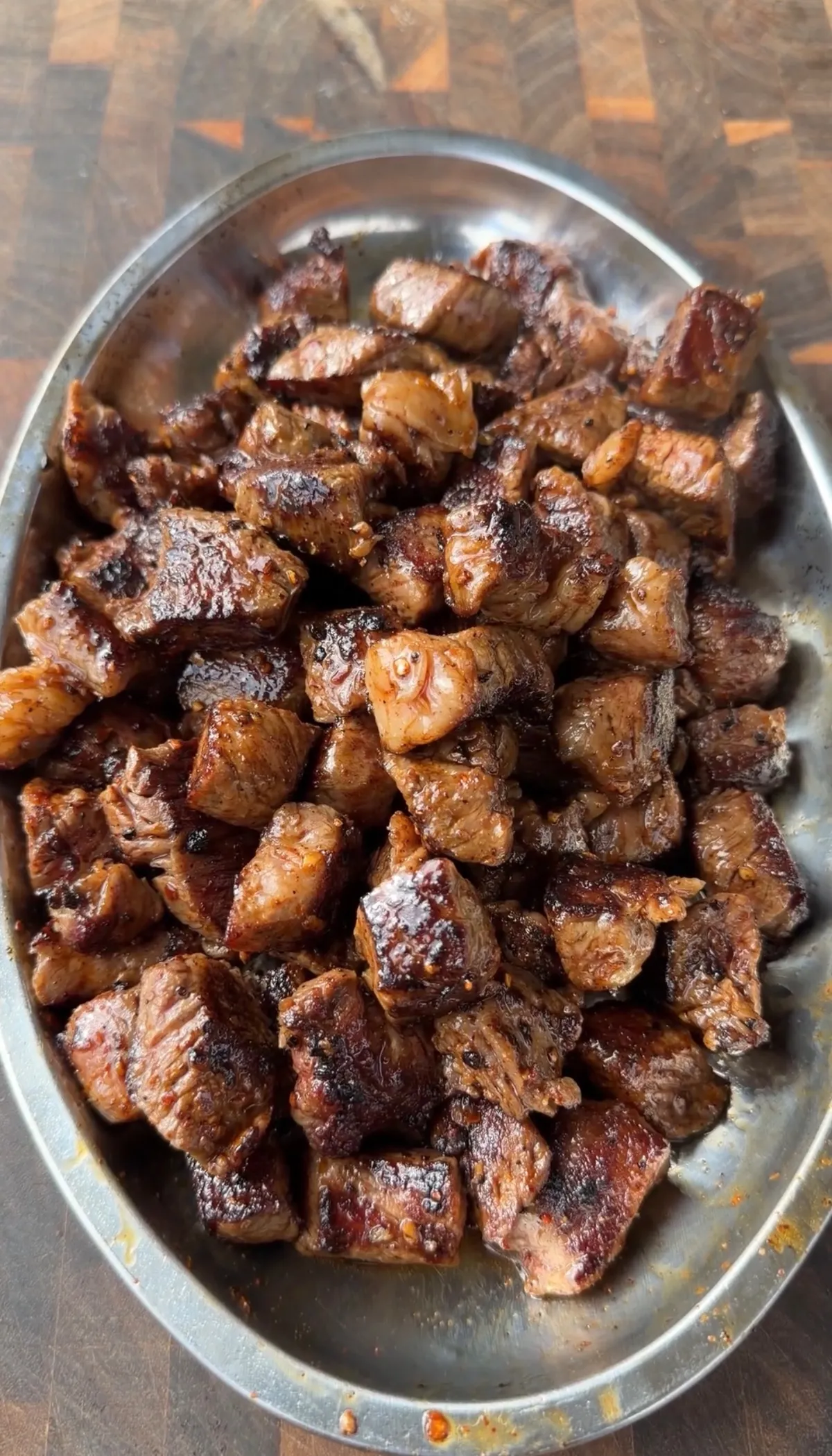 Seared ribeye steak bites with golden-brown crust piled high on a silver oval platter