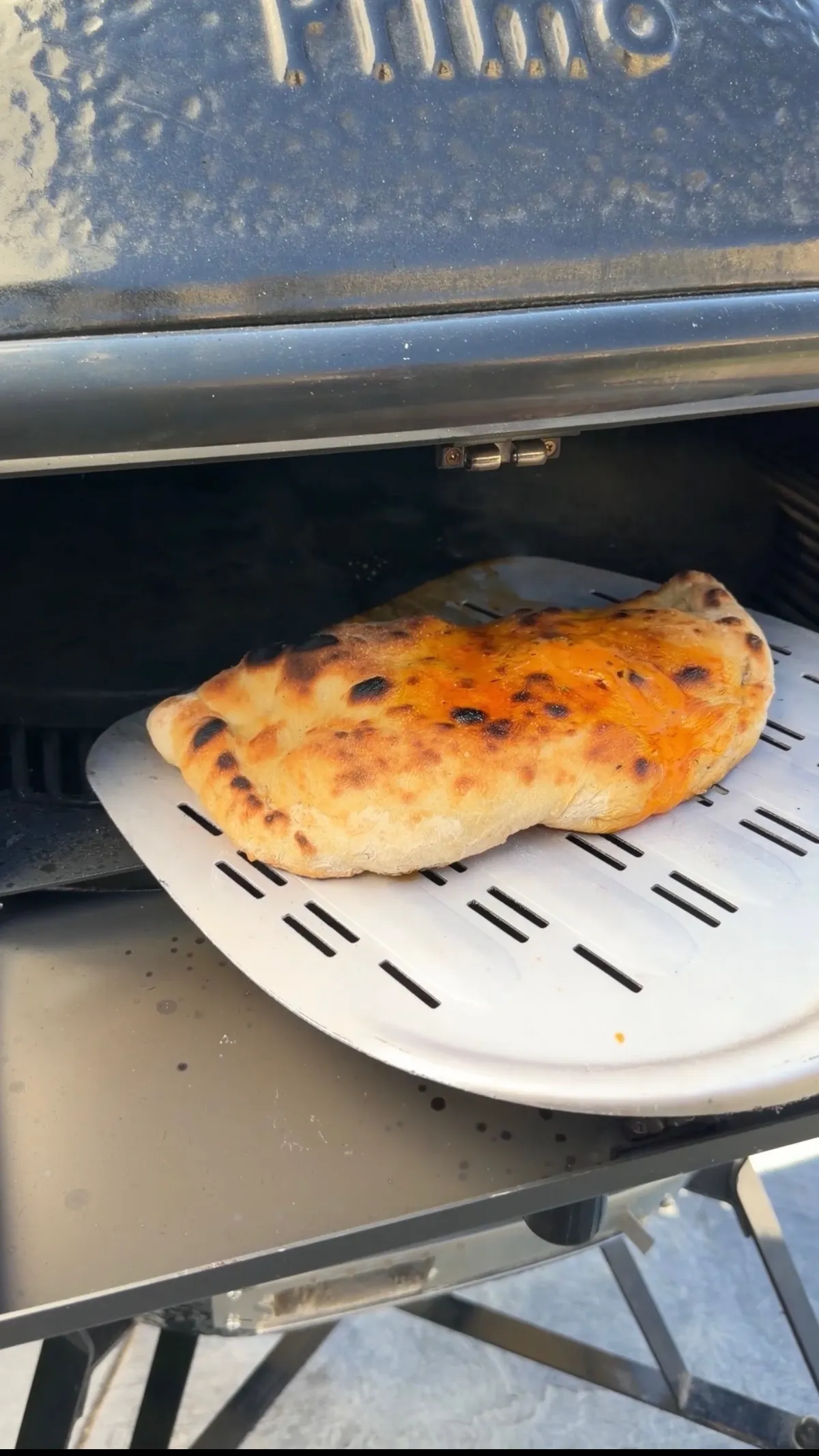 Golden-brown pepperoni calzone with crispy crust being pulled from a pizza oven on a perforated metal peel