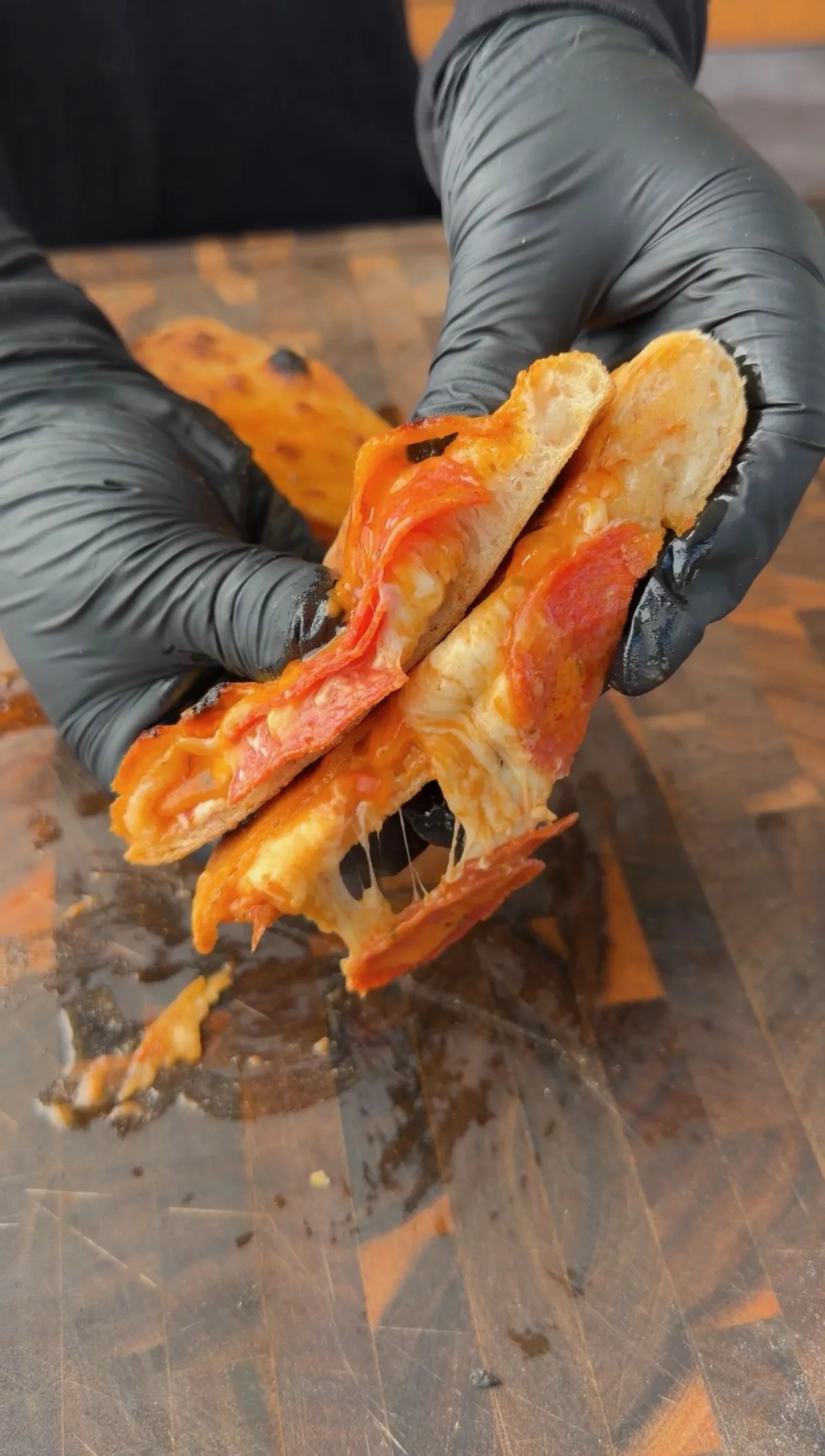 Gloved hands pulling apart a golden baked pepperoni calzone revealing stretchy fresh mozzarella and pizza sauce filling