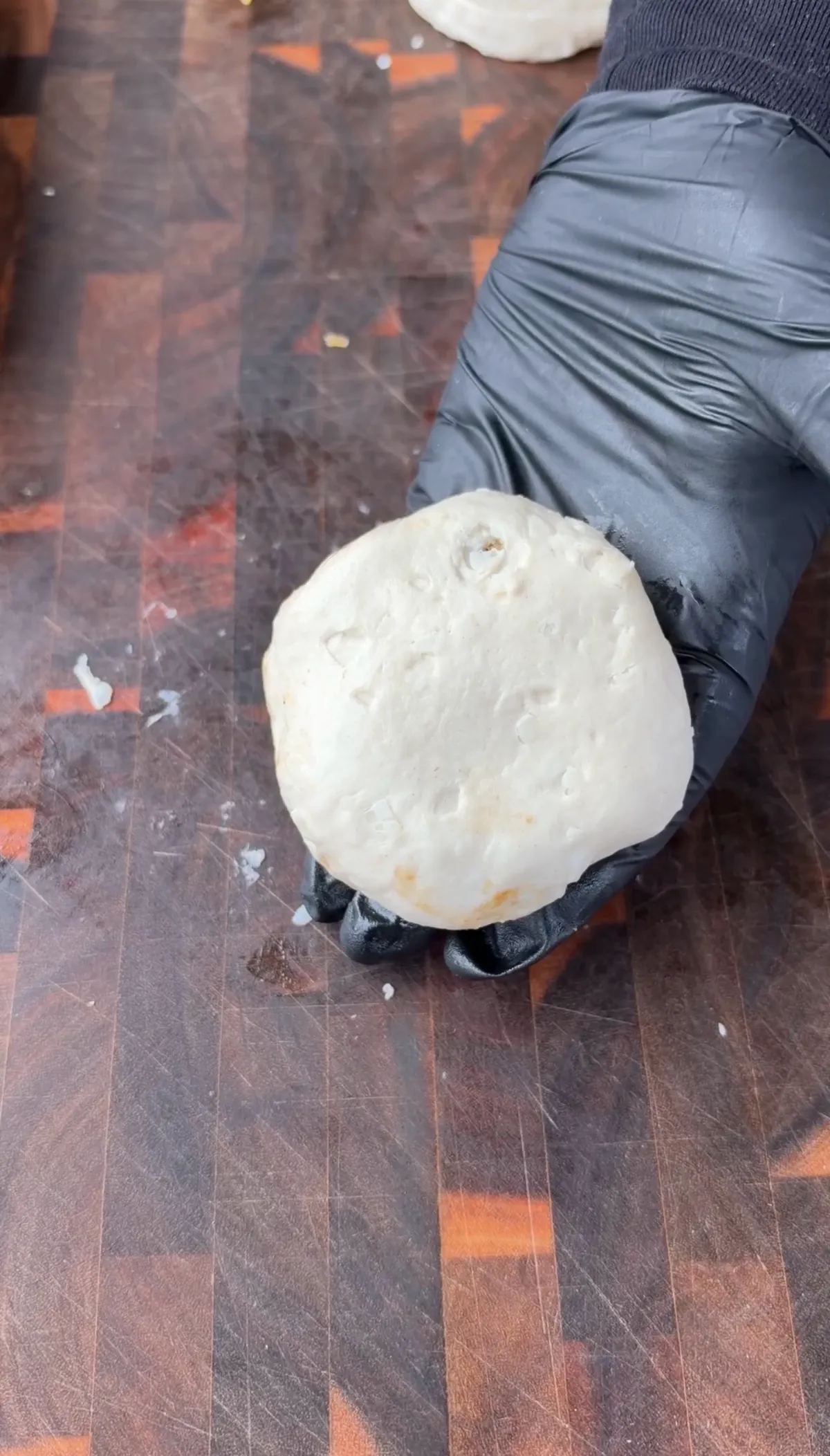 Gloved hand pressing sealed Pillsbury biscuit dough ball on wooden cutting board for smoked spicy cheeseburger bombs