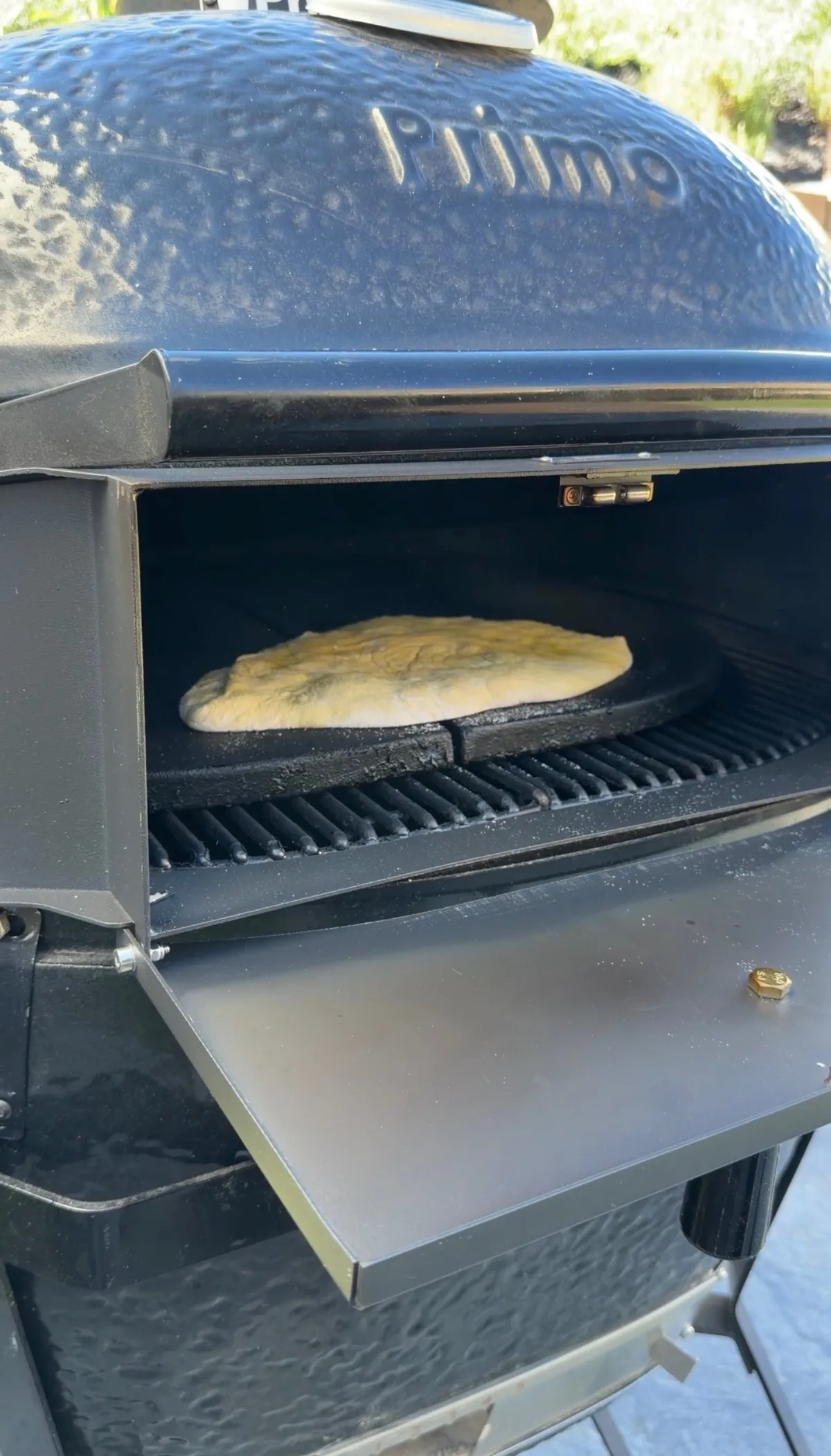 Folded pizza sandwich dough puffed and cooking on a cast iron pan inside a Primo pizza oven at 500–600°F