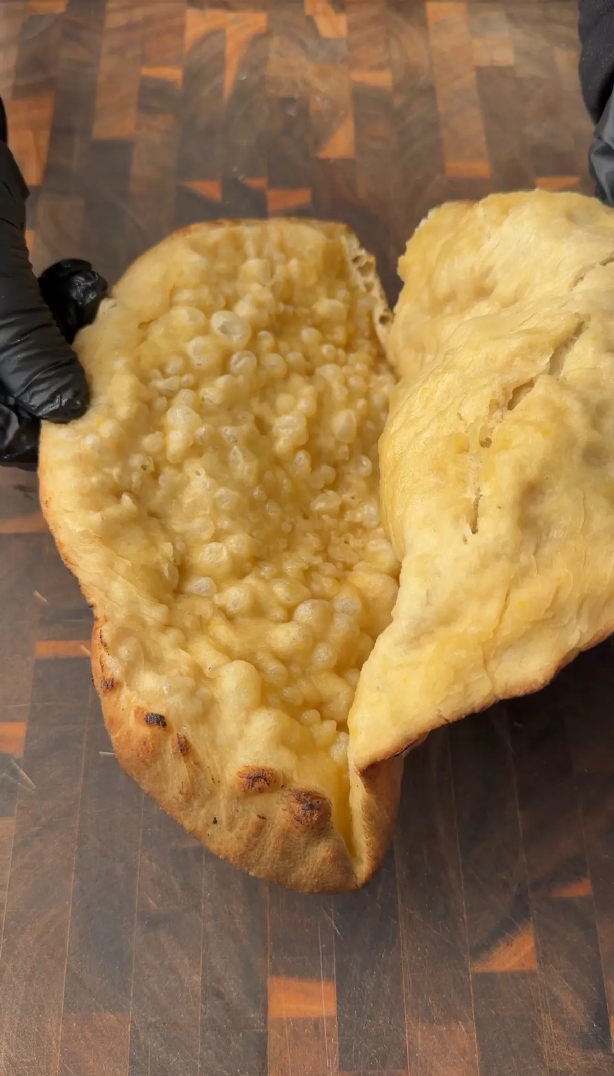 Folded pizza sandwich dough opened to reveal puffed, golden interior on a wooden cutting board