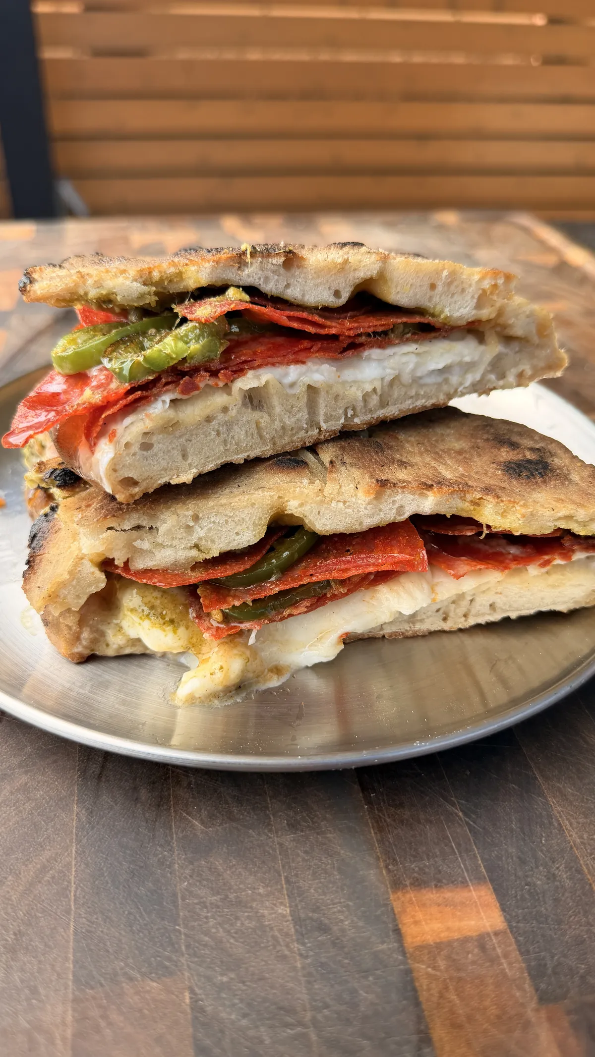 Pizza sandwich cut in half showing burrata, crispy pepperoni, charred jalapeños, hot honey, and pesto on a metal plate