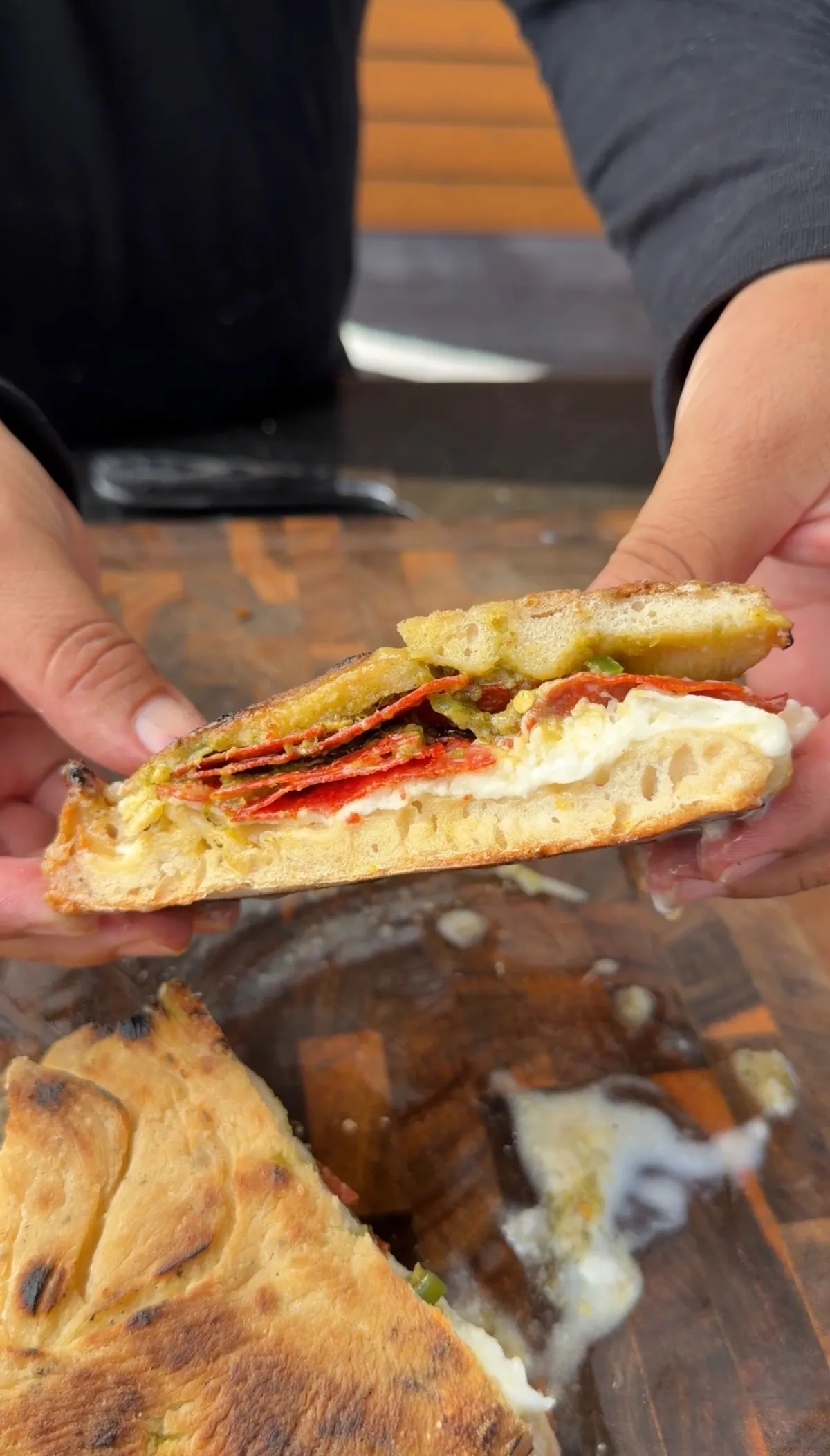 Pizza sandwich pulled open showing layers of burrata, crispy pepperoni, charred jalapeños, hot honey, and pesto on golden dough