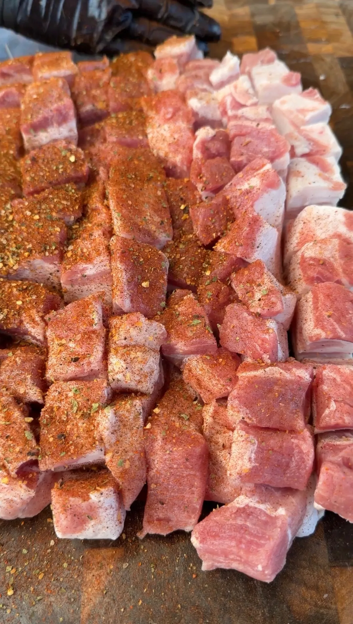 Pork belly strips scored and seasoned with ancho chili seasoning on a wooden cutting board, ready to roll into pinwheels