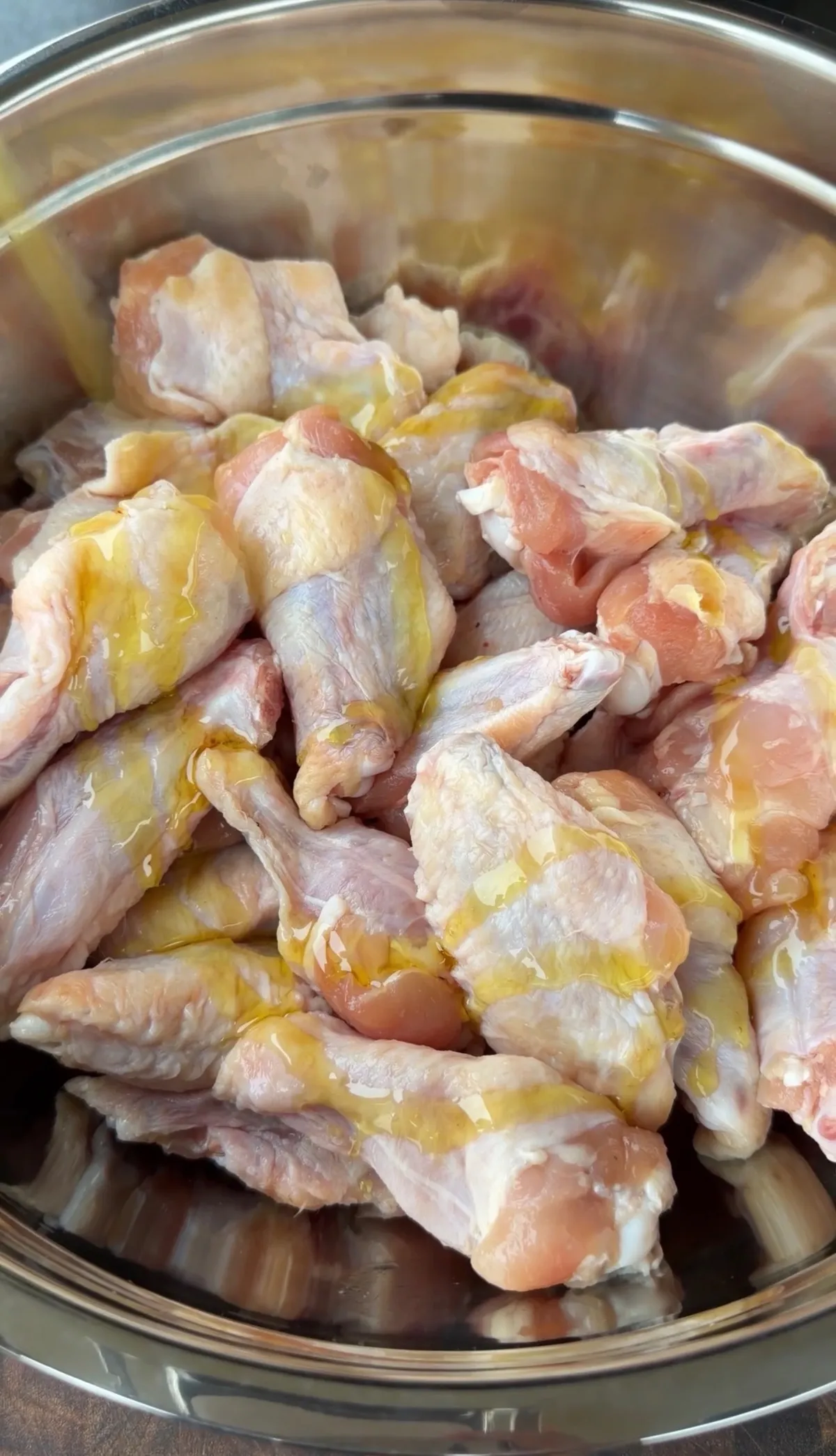 4 lbs of raw chicken wings coated with olive oil binder in a stainless steel mixing bowl, ready to season